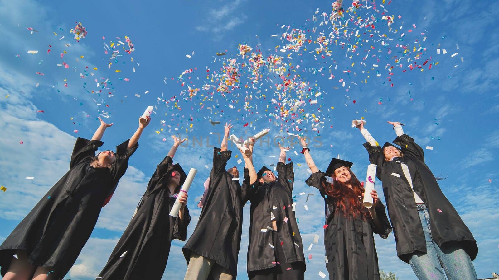 Graduates throw colorful confetti against a blue sky