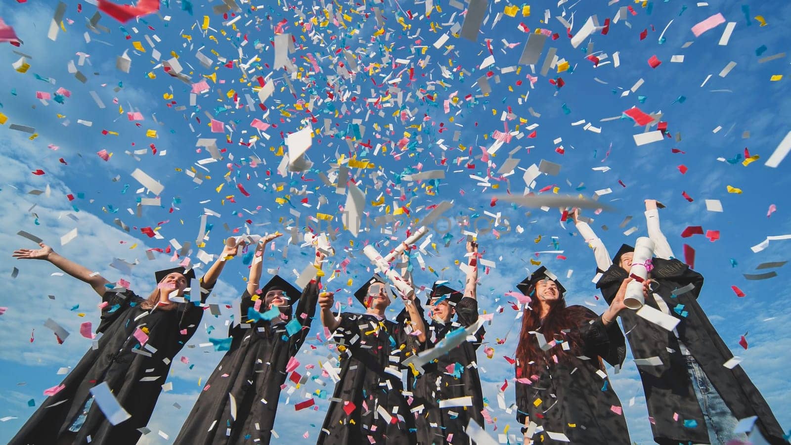 Happy graduates throw colorful confetti against a blue sky