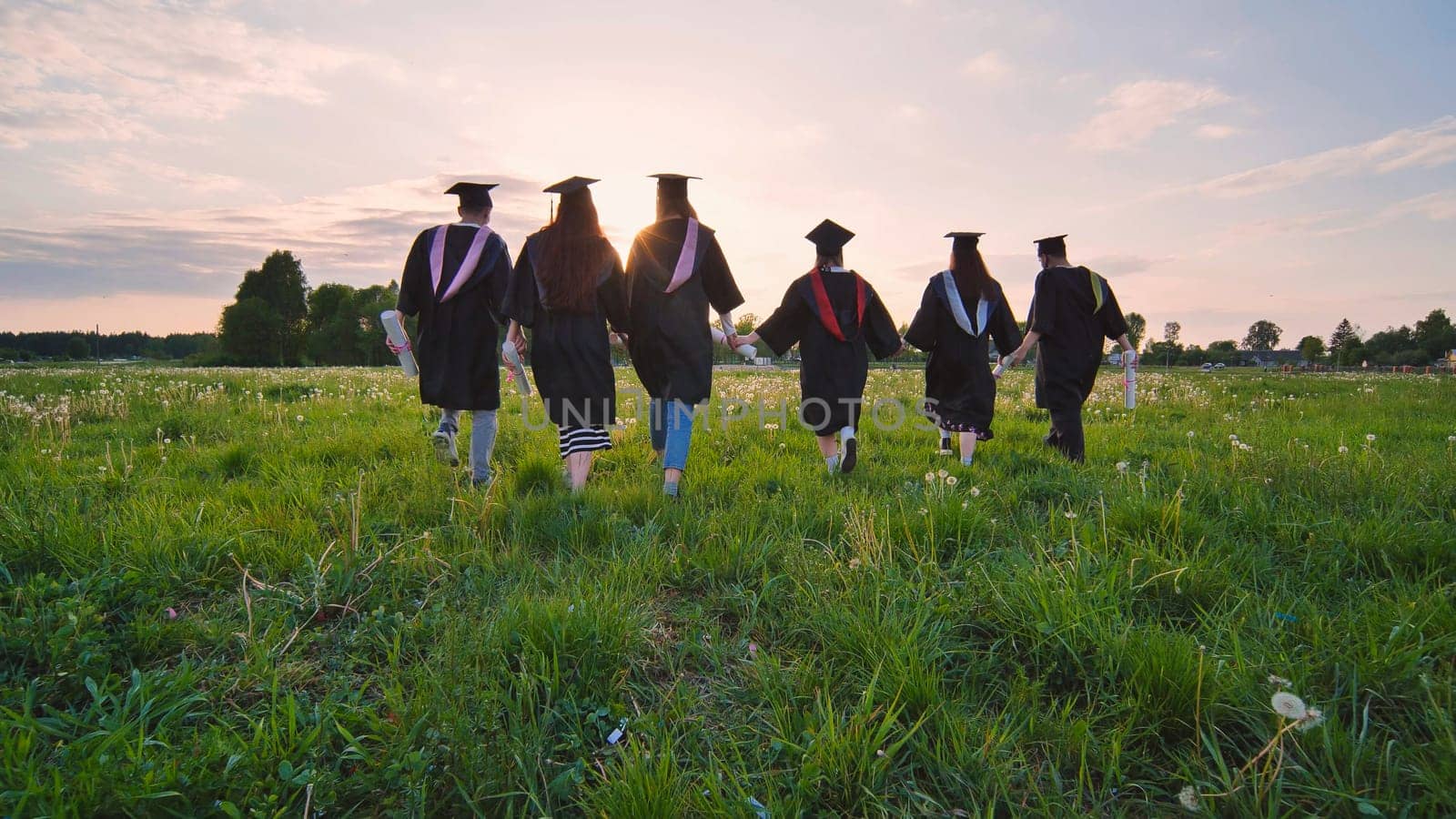Six graduates in robes walk towards the sun