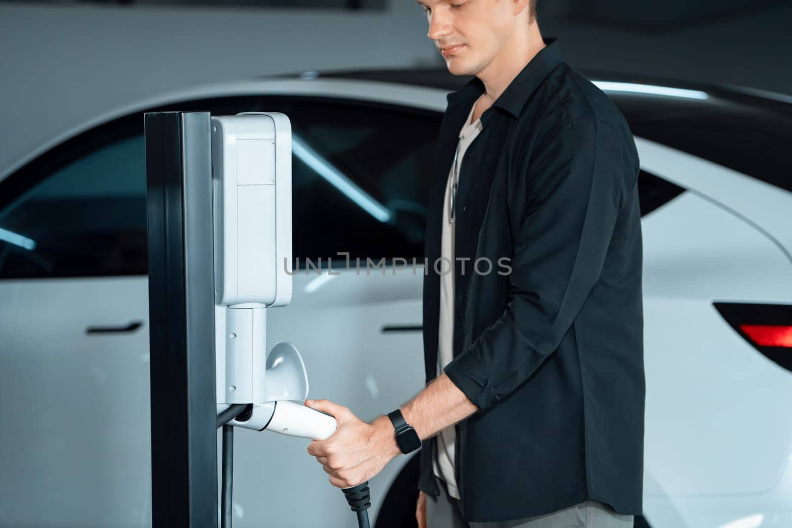 Young man travel with EV electric car to shopping center parking lot charging in downtown city showing urban sustainability lifestyle by green clean rechargeable energy of electric vehicle innards