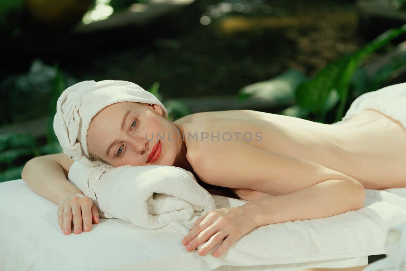 Portrait of young attractive caucasian women with beautiful skin lies on spa bed while waiting for body massage surrounded by relaxing natural environment. Healthy and beauty concept. Tranquility.