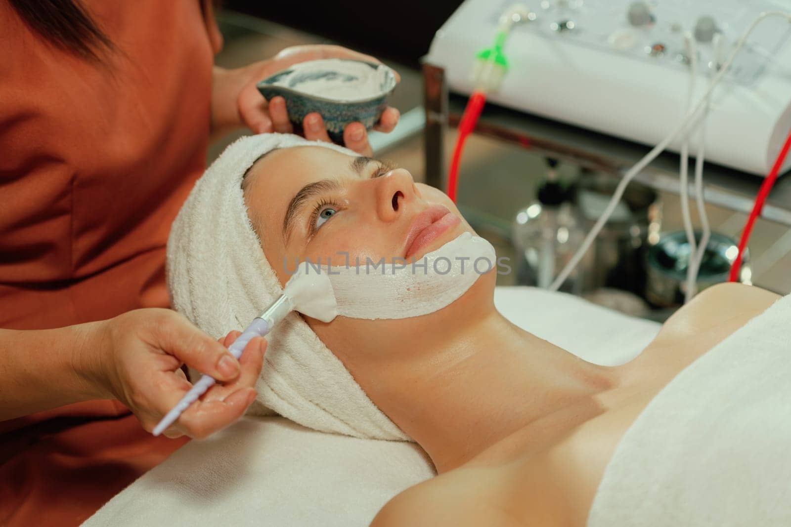 Beautiful young women lie on spa bed while having facial massage from professional doctor. Attractive female with beautiful skin surrounded by electric facial machine. Tranquility.