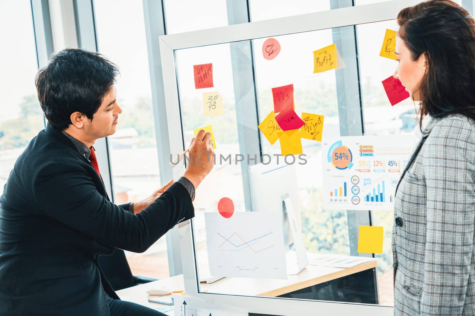 Business people work on project planning board in office and having conversation with coworker friend to analyze project development . They use sticky notes posted on glass to make it organized. Jivy