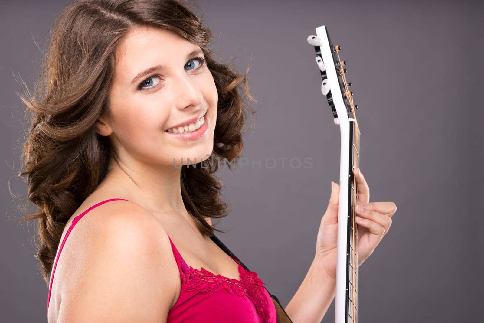 Young and smiling girl with guitar against gray background