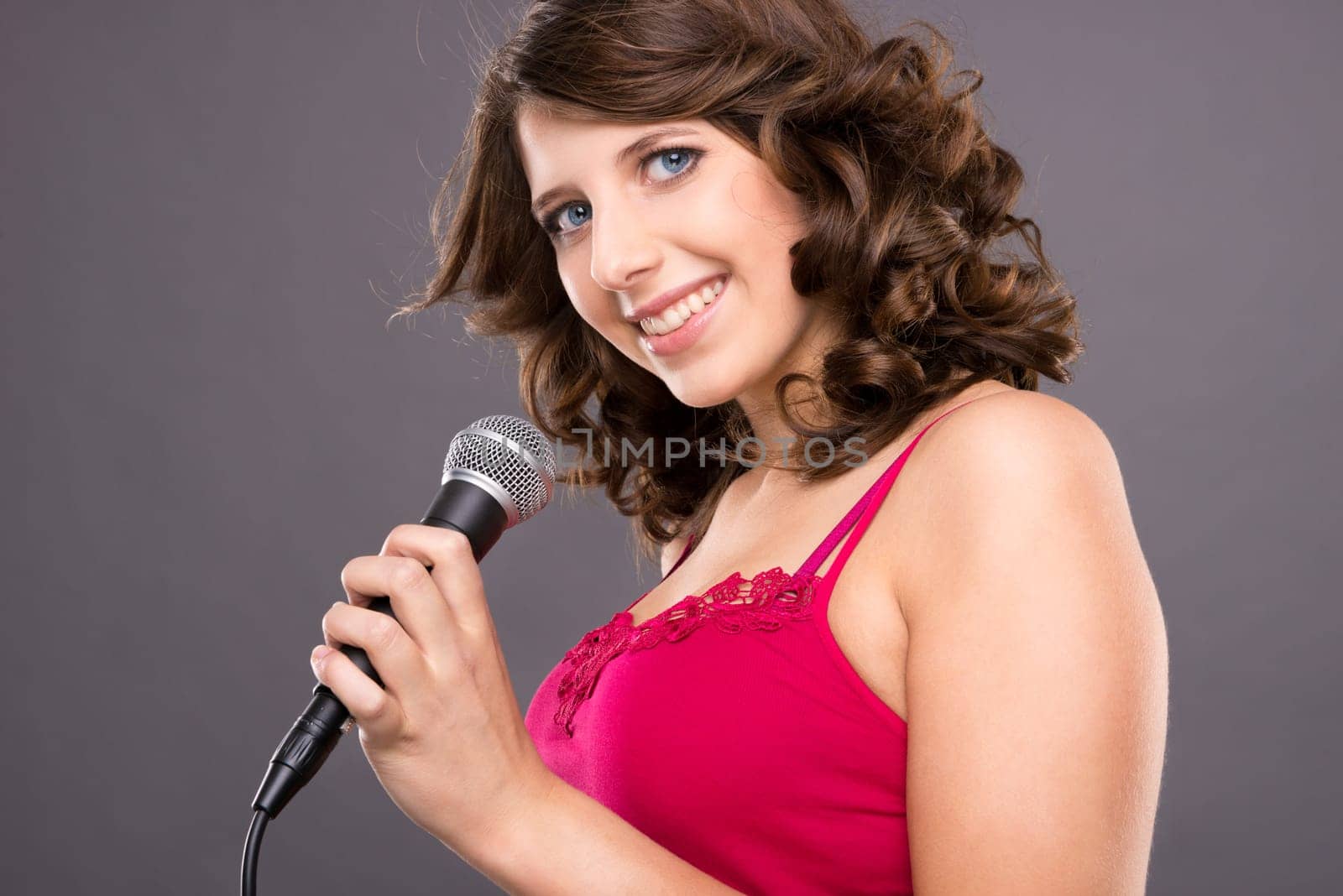 Young and smiling girl with microphone against gray background
