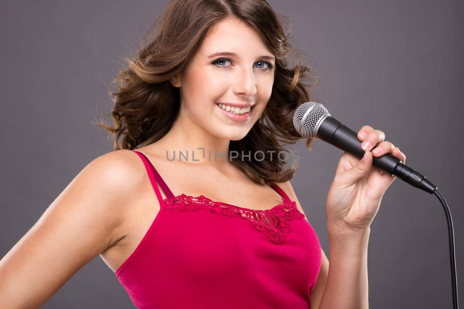 Young and smiling girl with microphone against gray background