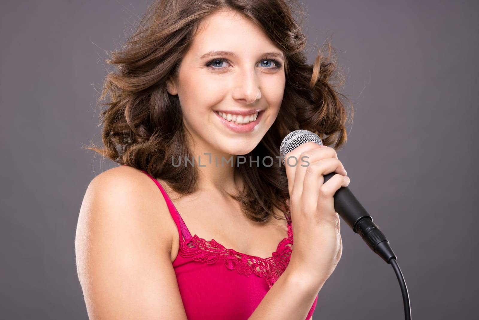 Young and smiling girl with microphone against gray background