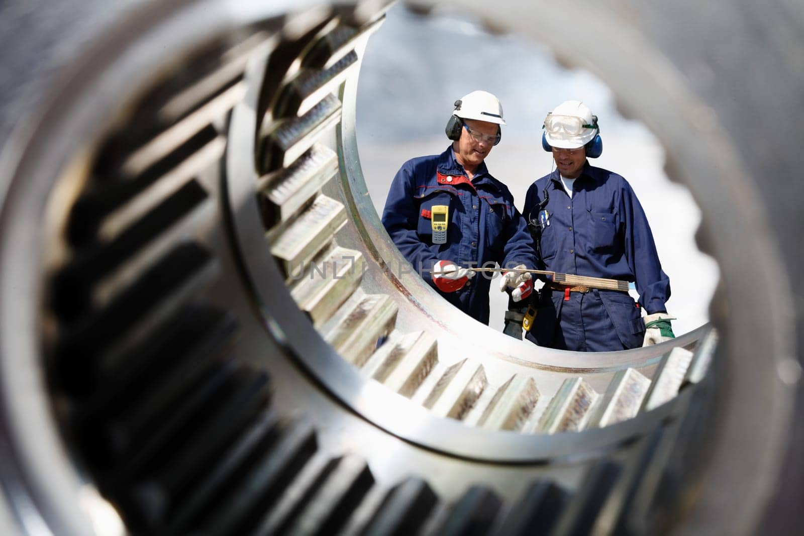 two mechanics, engineers seen through a large cogwheels axle
