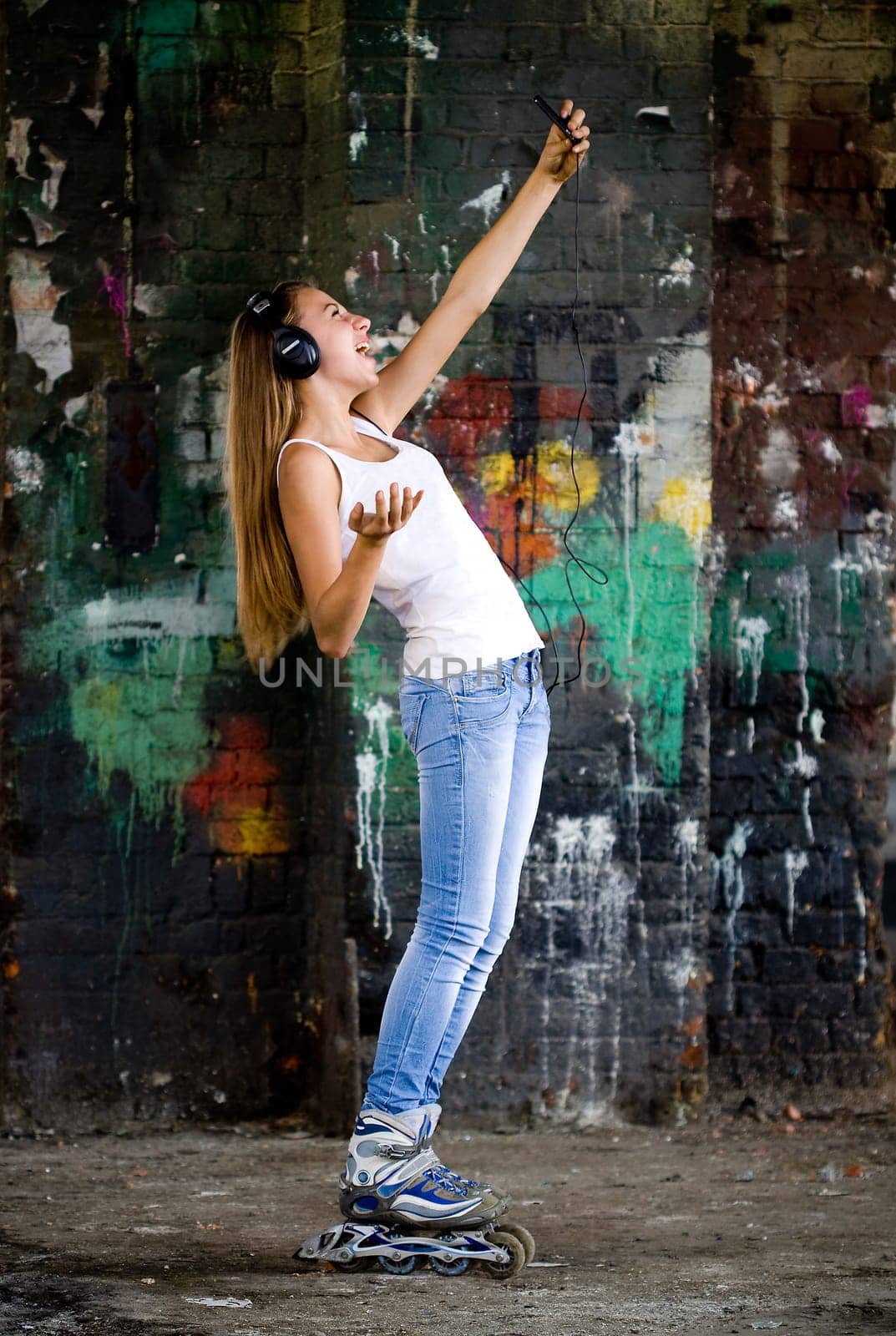 Young girl with headphones and roller shoes at graffiti wall
