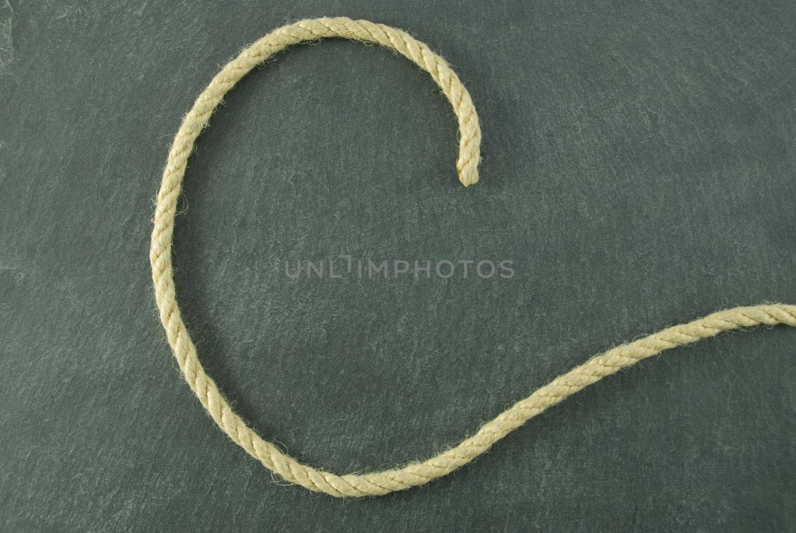 a C of rope lying on a slate table, symbolizing education and writing