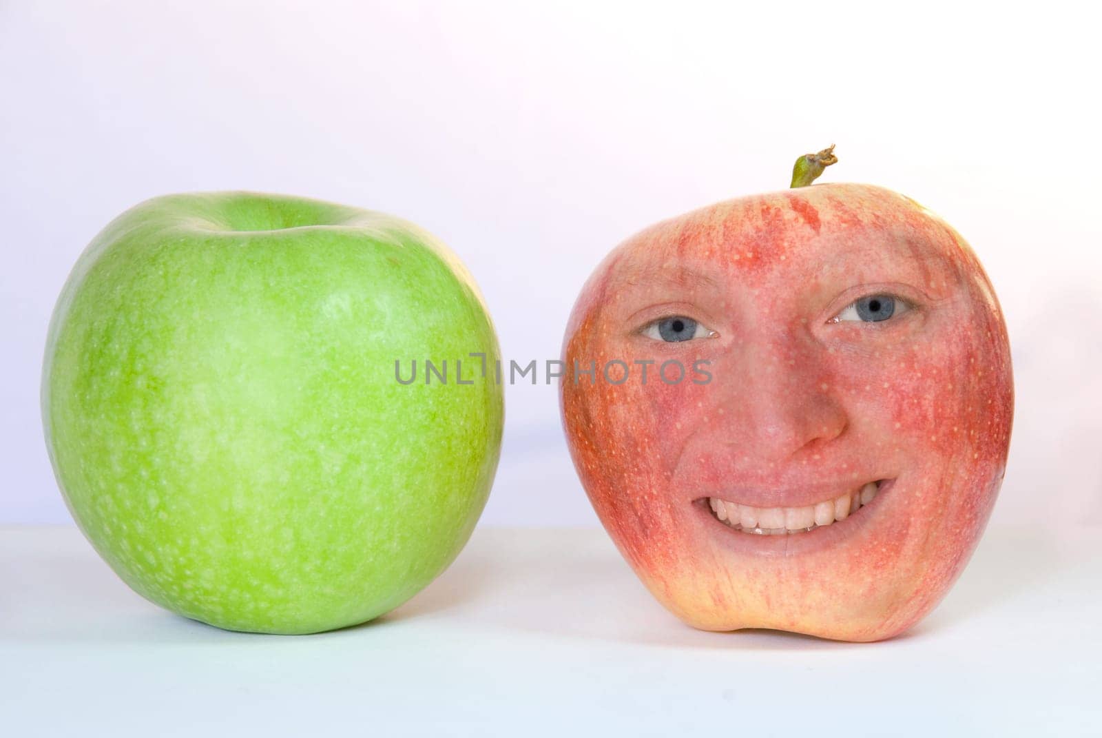 a green and a red apple. The red apple has a smiling face on it.