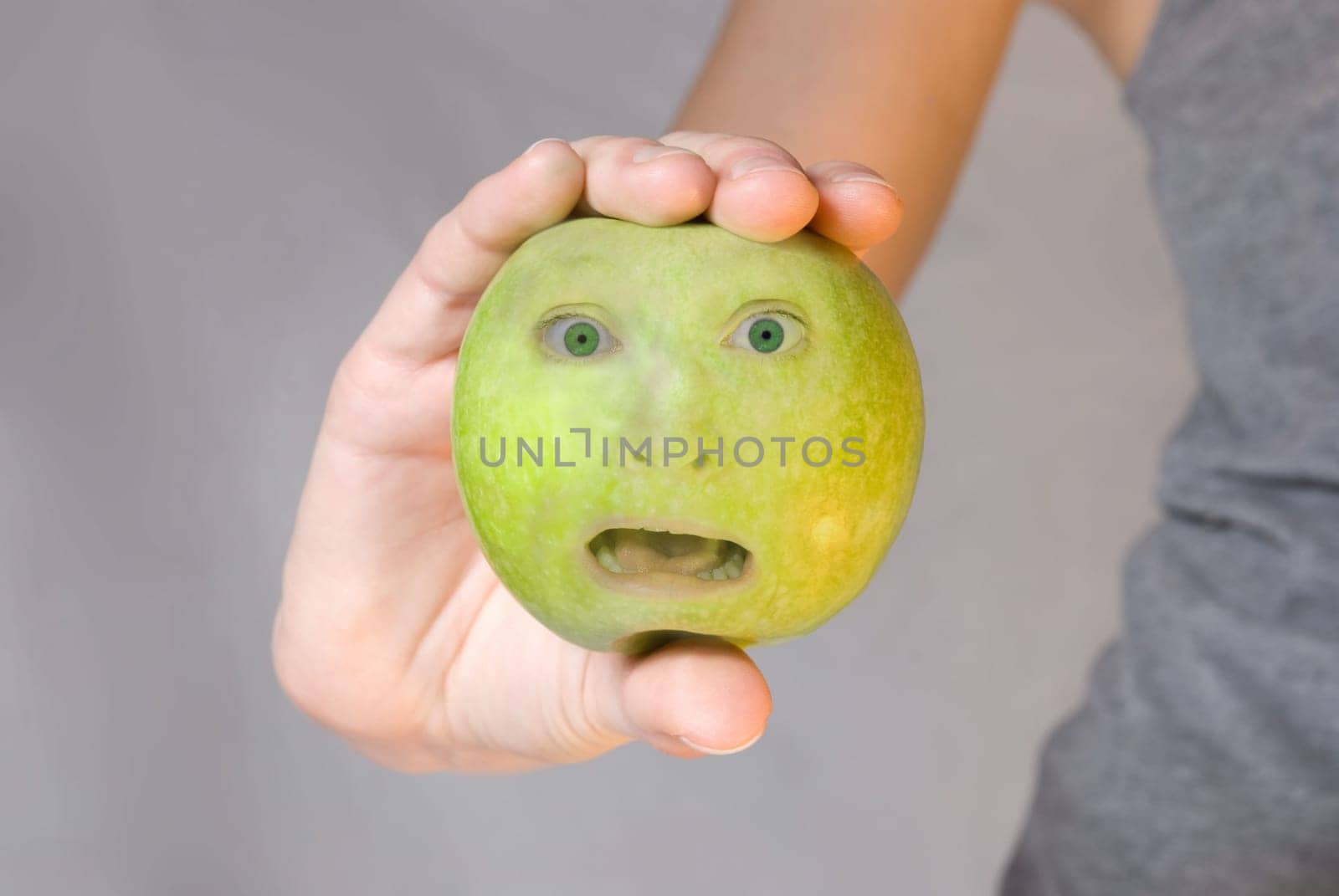 hands holds an green apple with a fearful looking face on it