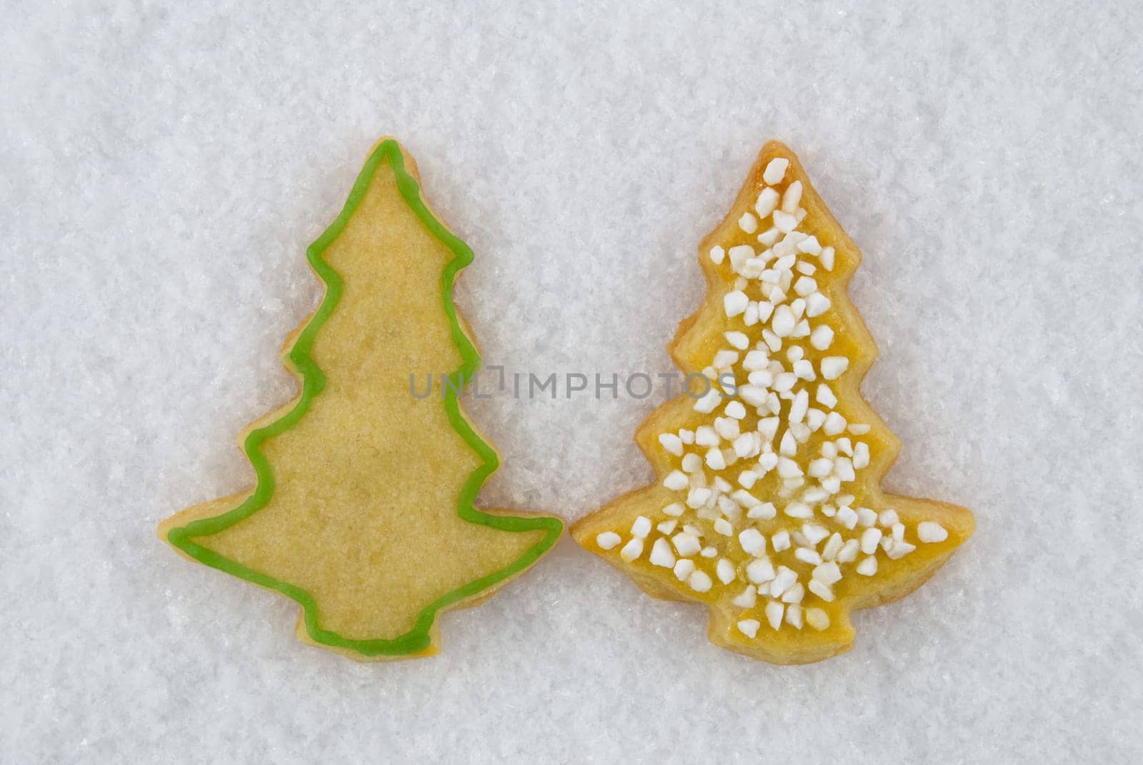 two christmas tree cookies lying next to each other in the snow