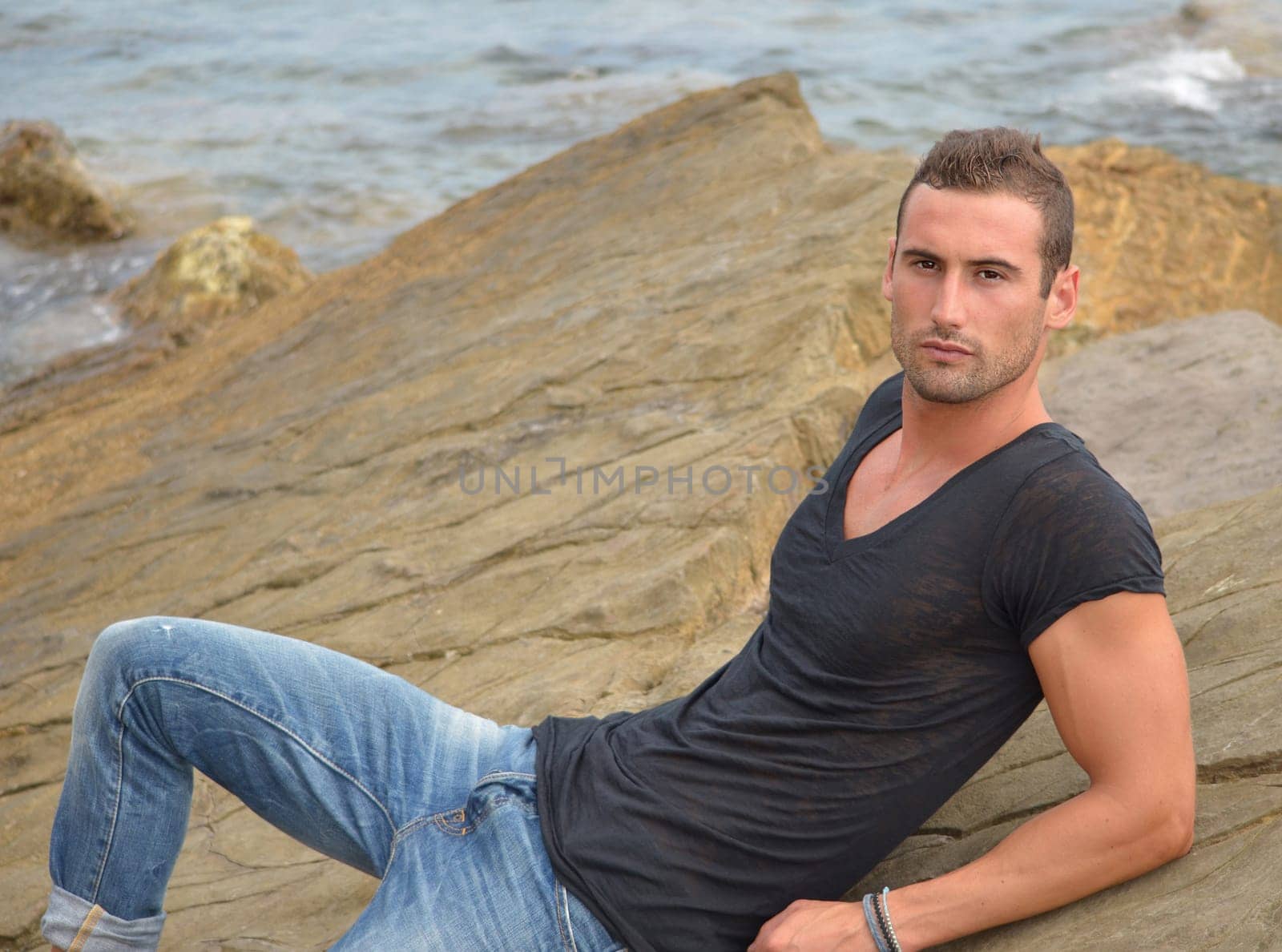 Attractive and athletic young man sitting or laying on a rock
