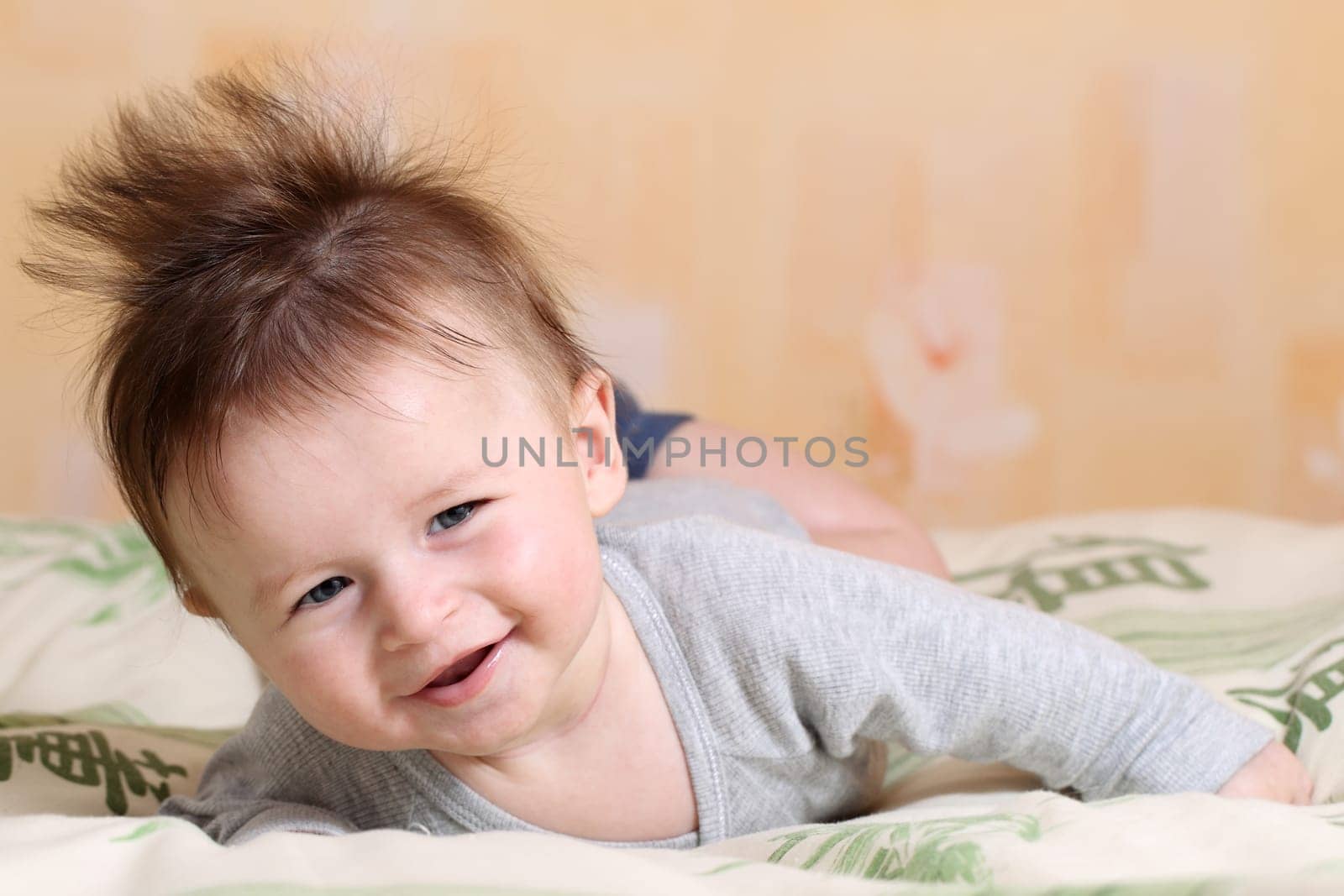Portrait of a baby 4 months old lying on his belly with mohawk hairstyle.