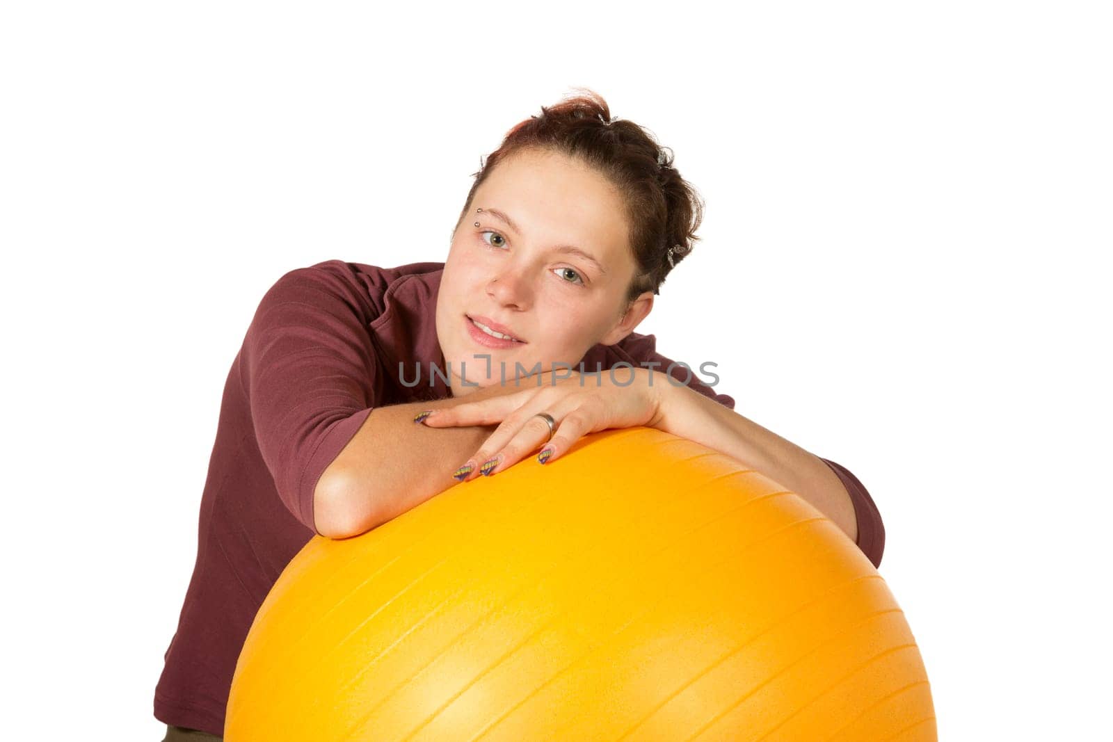 Beautiful young woman relaxing with her arms resting on top of a yellow pilates ball isolated on white