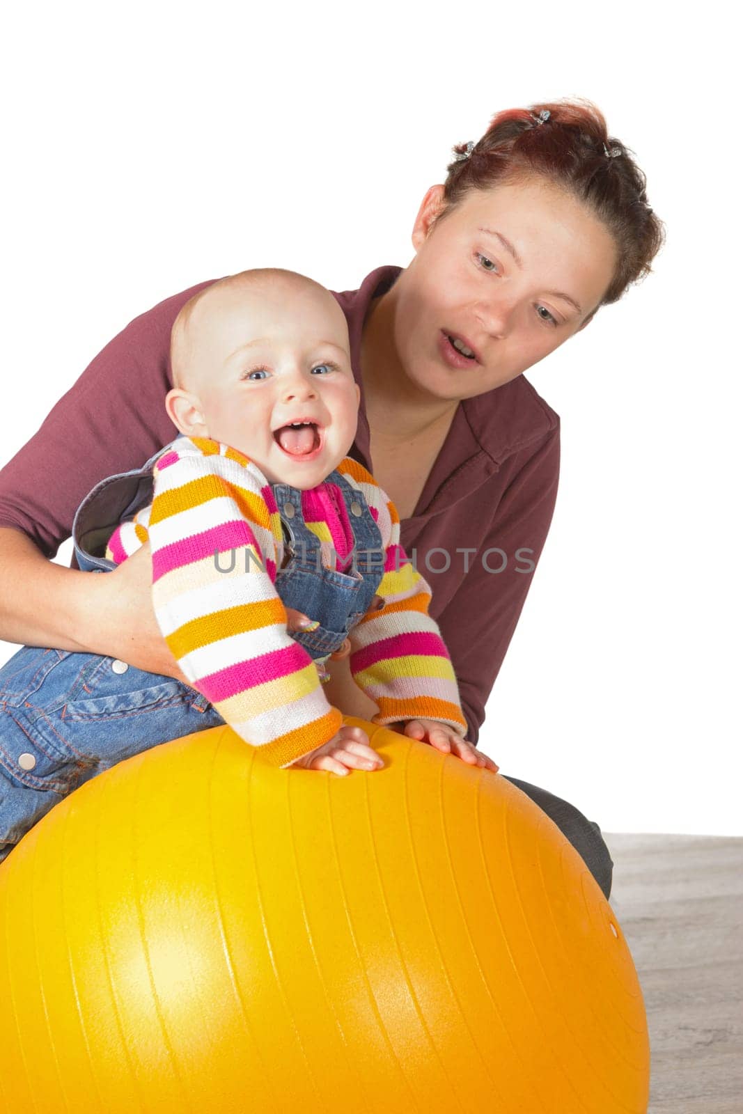 Laughing baby with delayed motor activity development doing exercises with the support of its mother and a yellow gym ball to strengthen muscles and develop coordination of motion