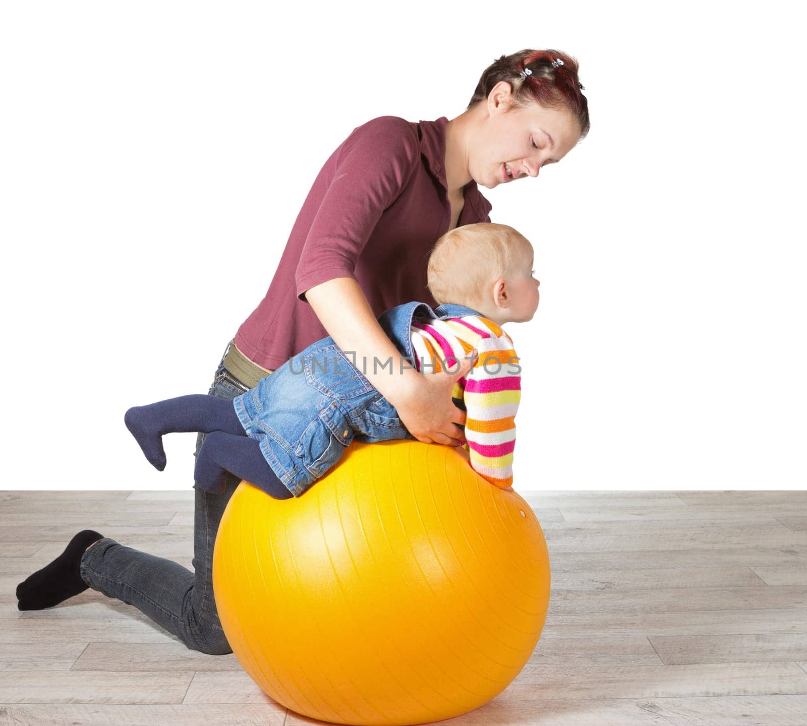 Mother exercising her young baby supporting it over a gym ball to stimulate muscle coordination and motion due to late development of motor skills