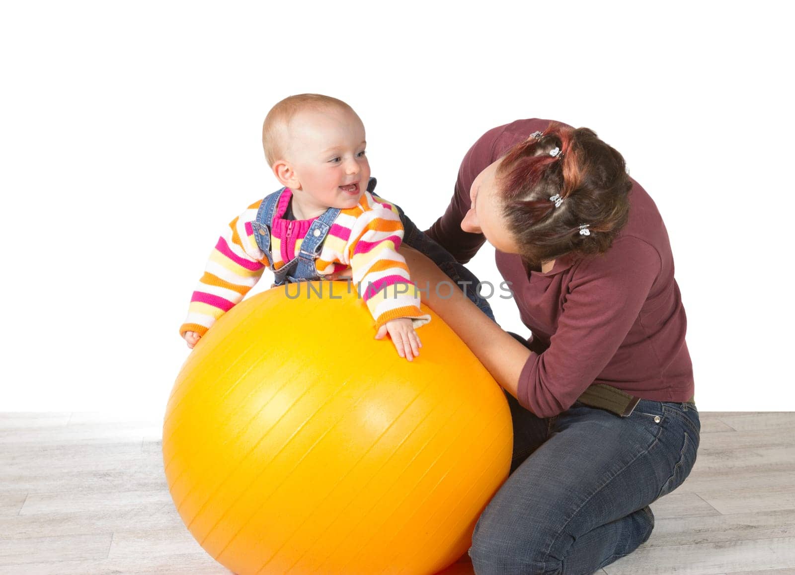 Devoted mother exercising her laughing baby who has late development of motor activity using a yellow pilates ball