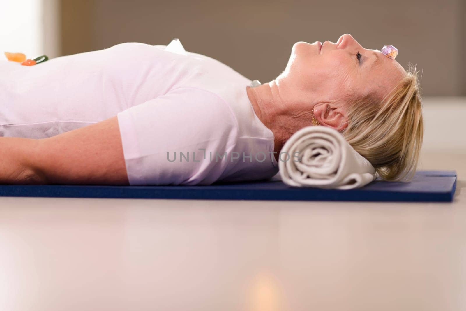 Senior woman relaxing and lying on pad with amethyst, quartz and other crystals on body. Side view, copy space