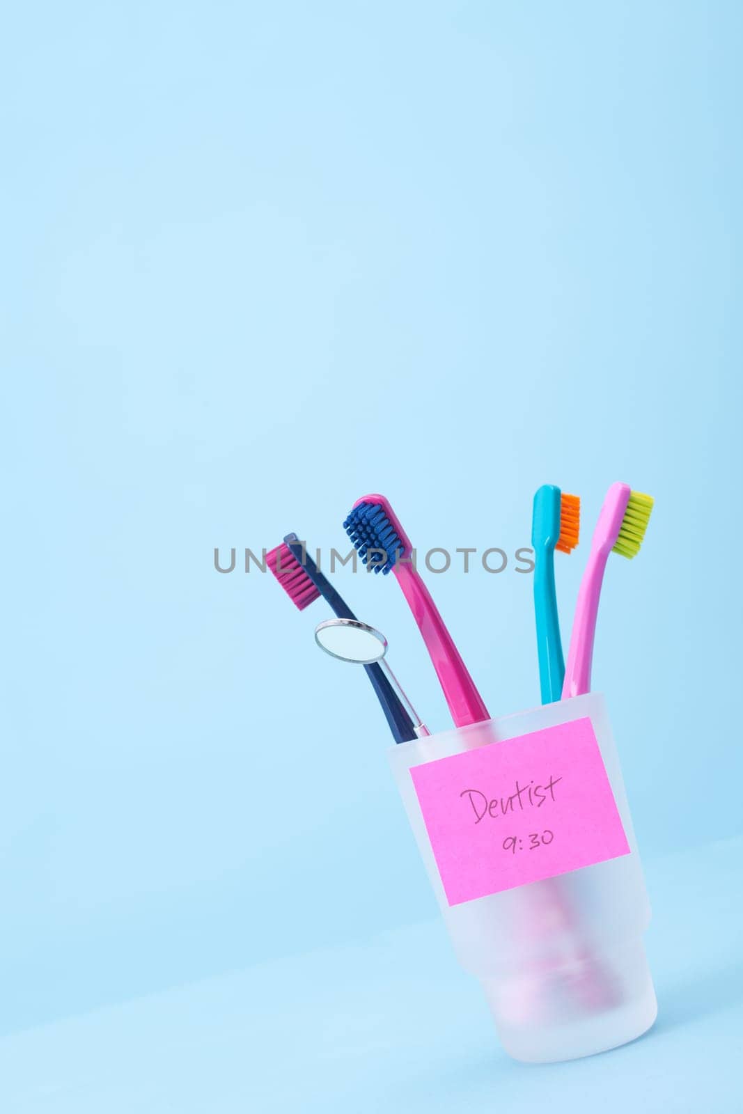 Dentist visit concept - four toothbrushes, speculum and sticky note reminder. Selective focused on sticky note reminder, blue background.