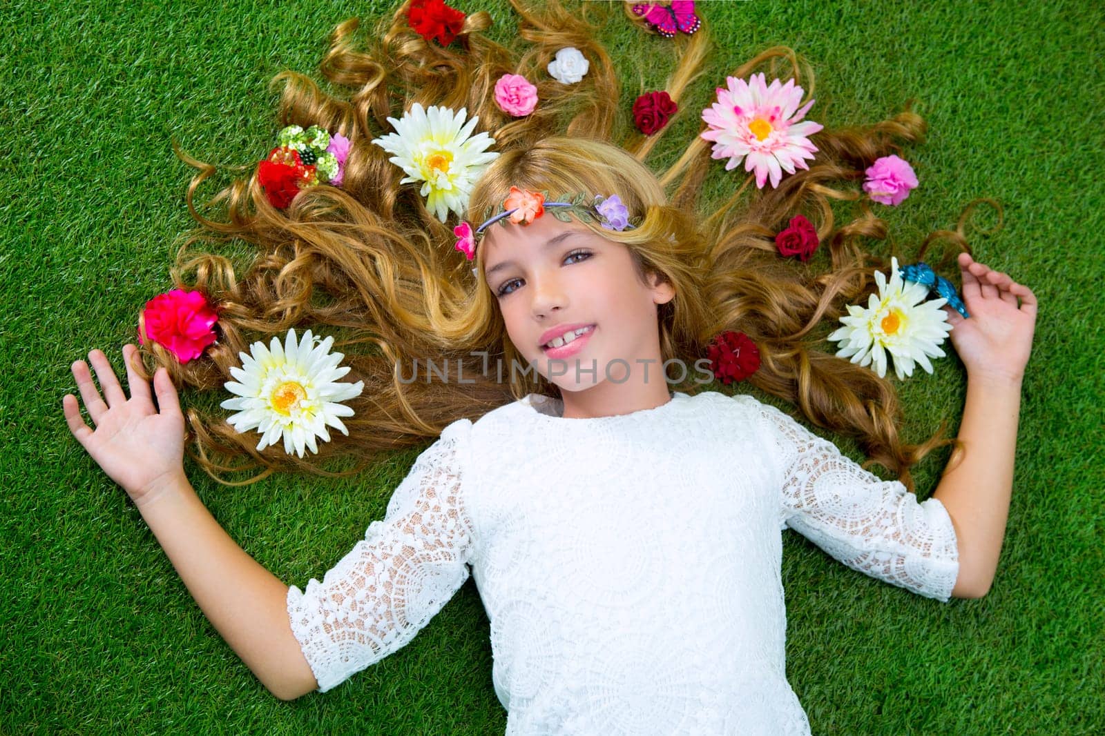 Blond spring children girl with flowers on hair over green grass floor