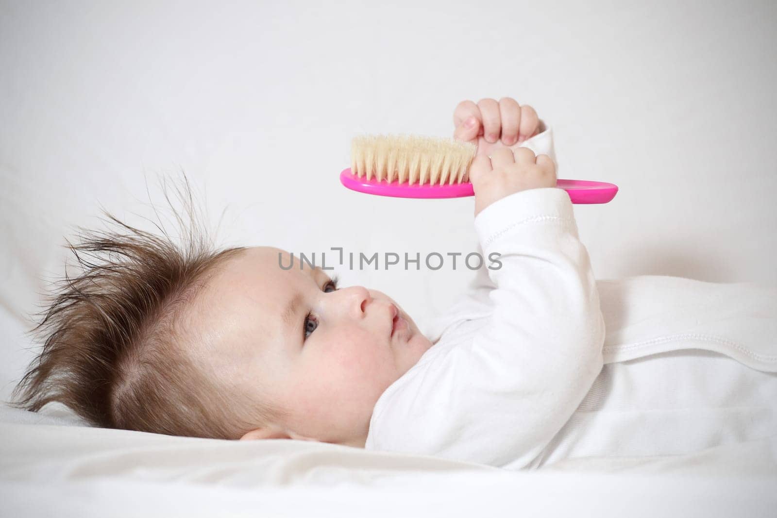 Portrait of a playing baby with a hairbrush, lying down on back