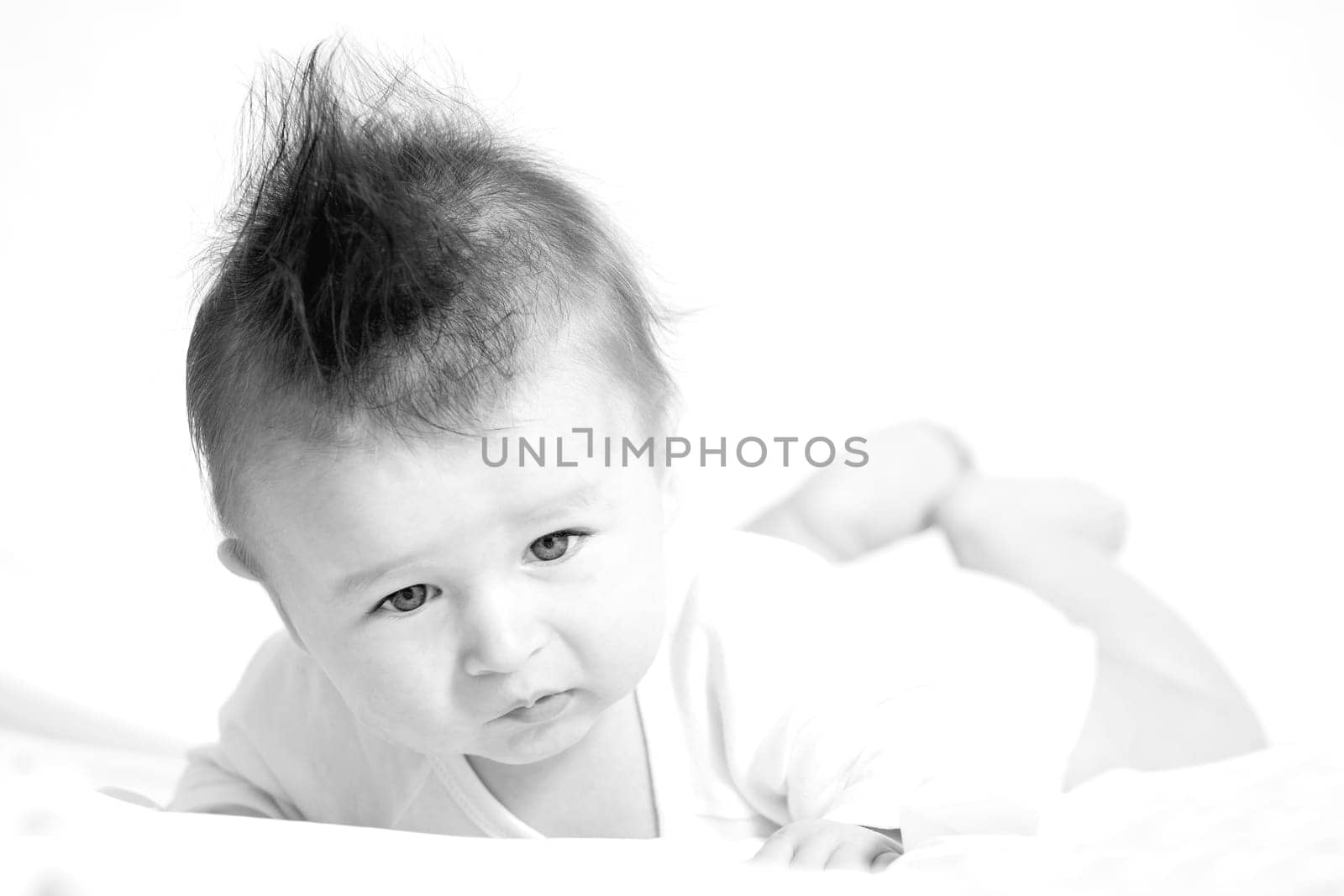 Portrait of a baby 4 months old lying on his belly with mohawk hairstyle.