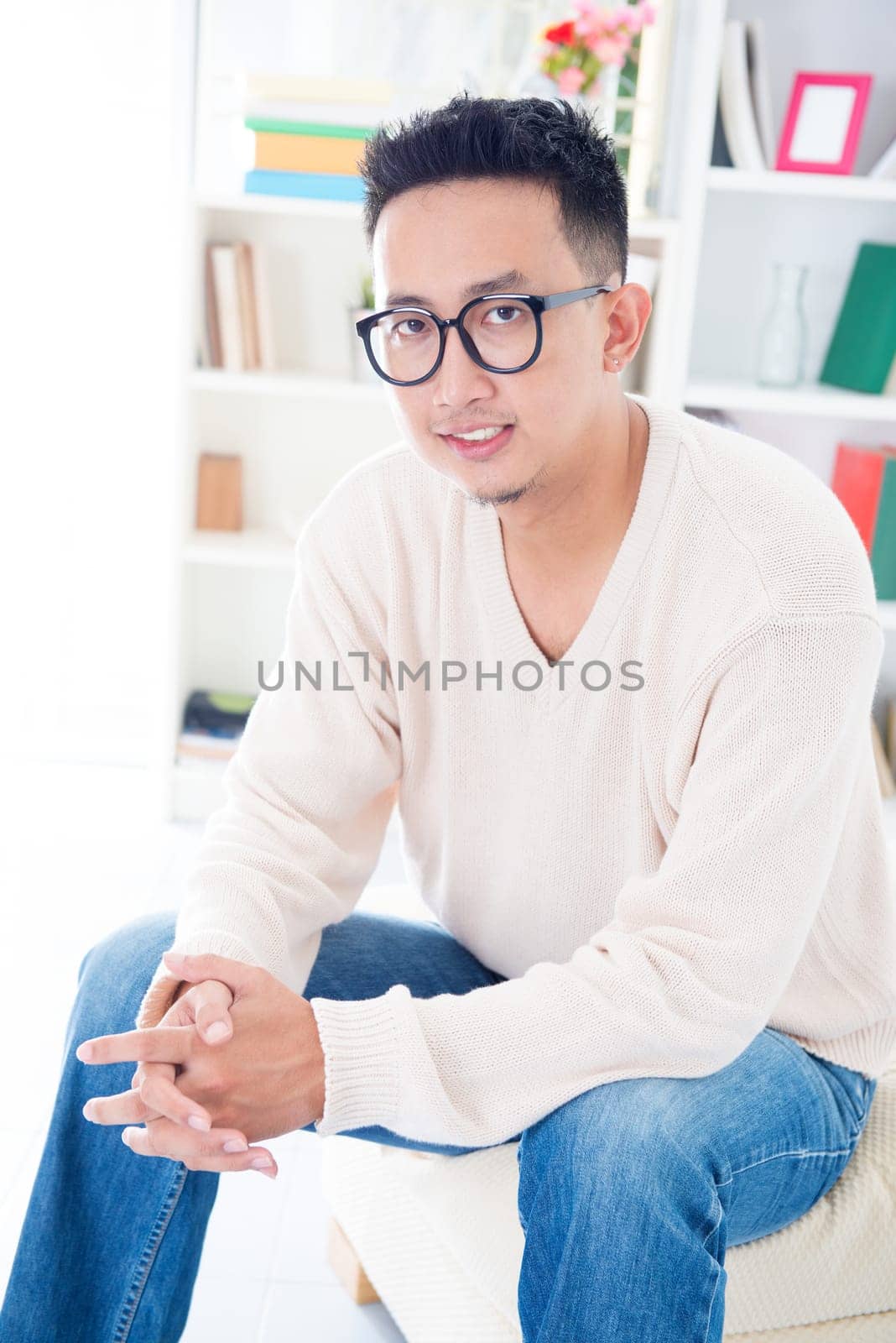 Southeast Asian male with spectacles sitting on sofa at home, indoor living lifestyle