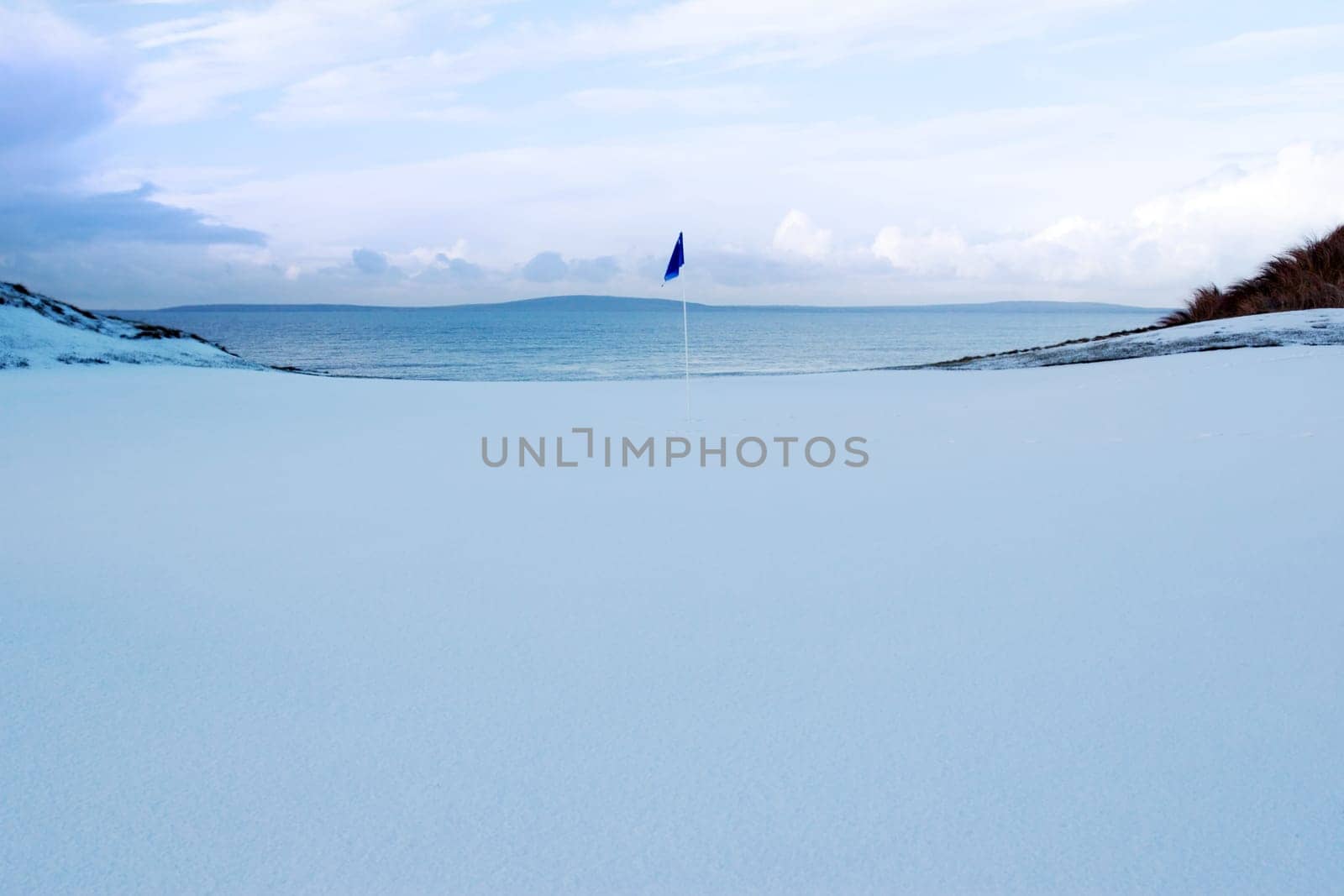 a snow covered links golf hole in ireland in winter weather with blue flag