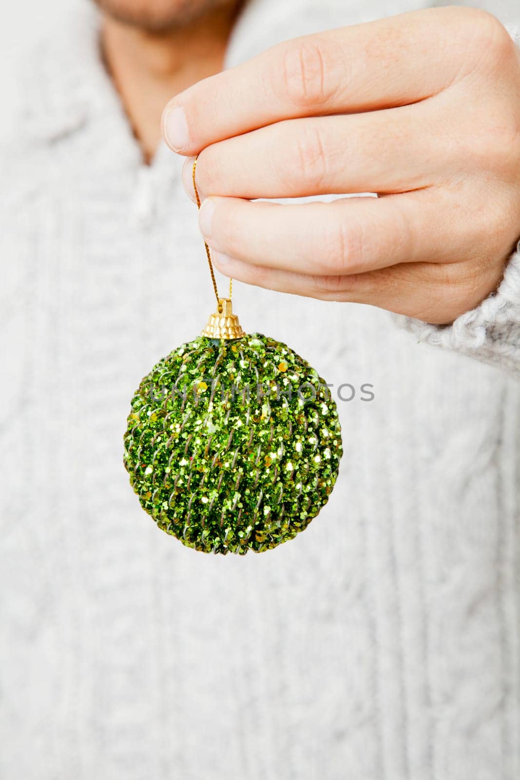 Closeup of green Christmas bauble hanging from fingers
