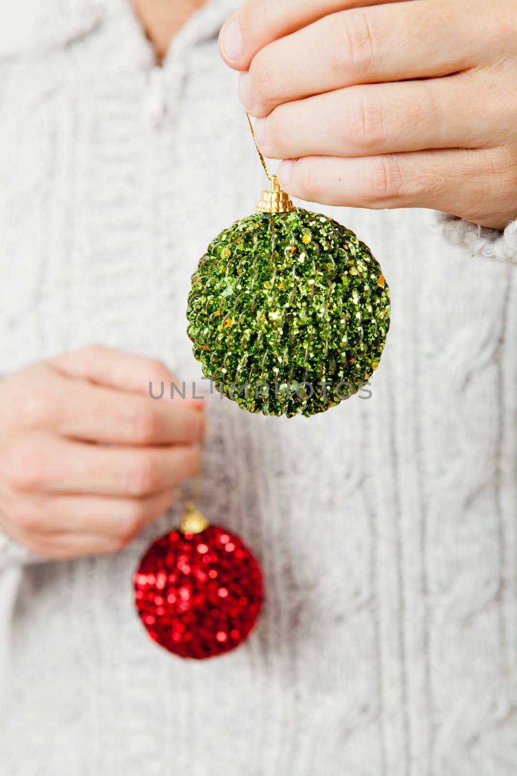 Closeup of red and green Christmas baubles hanging from fingers