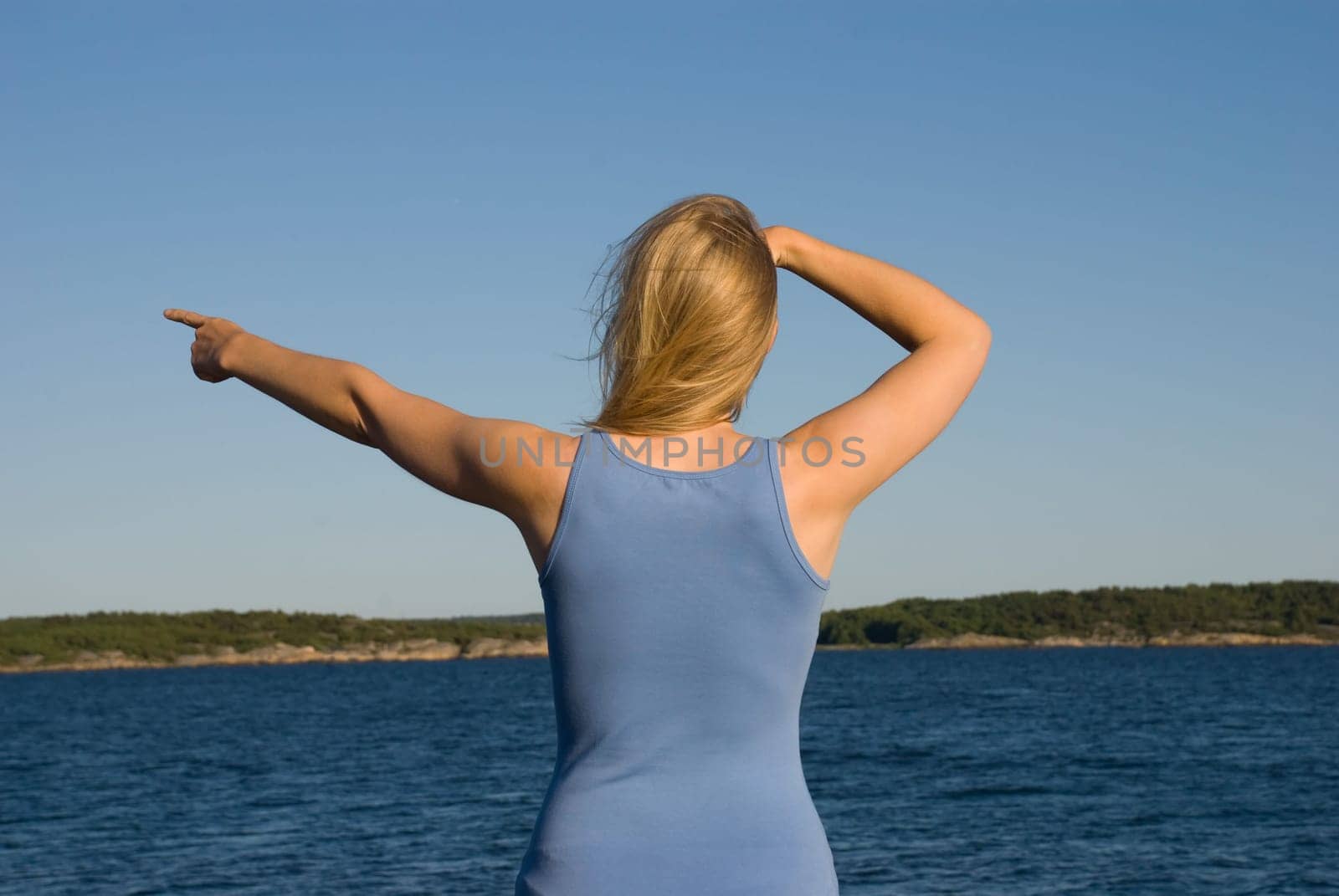 a young european looking woman in blue cloth standing at the coast of the ocean shows something