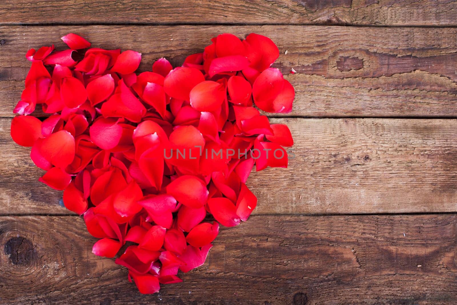 Rose petals as a heart on wooden board