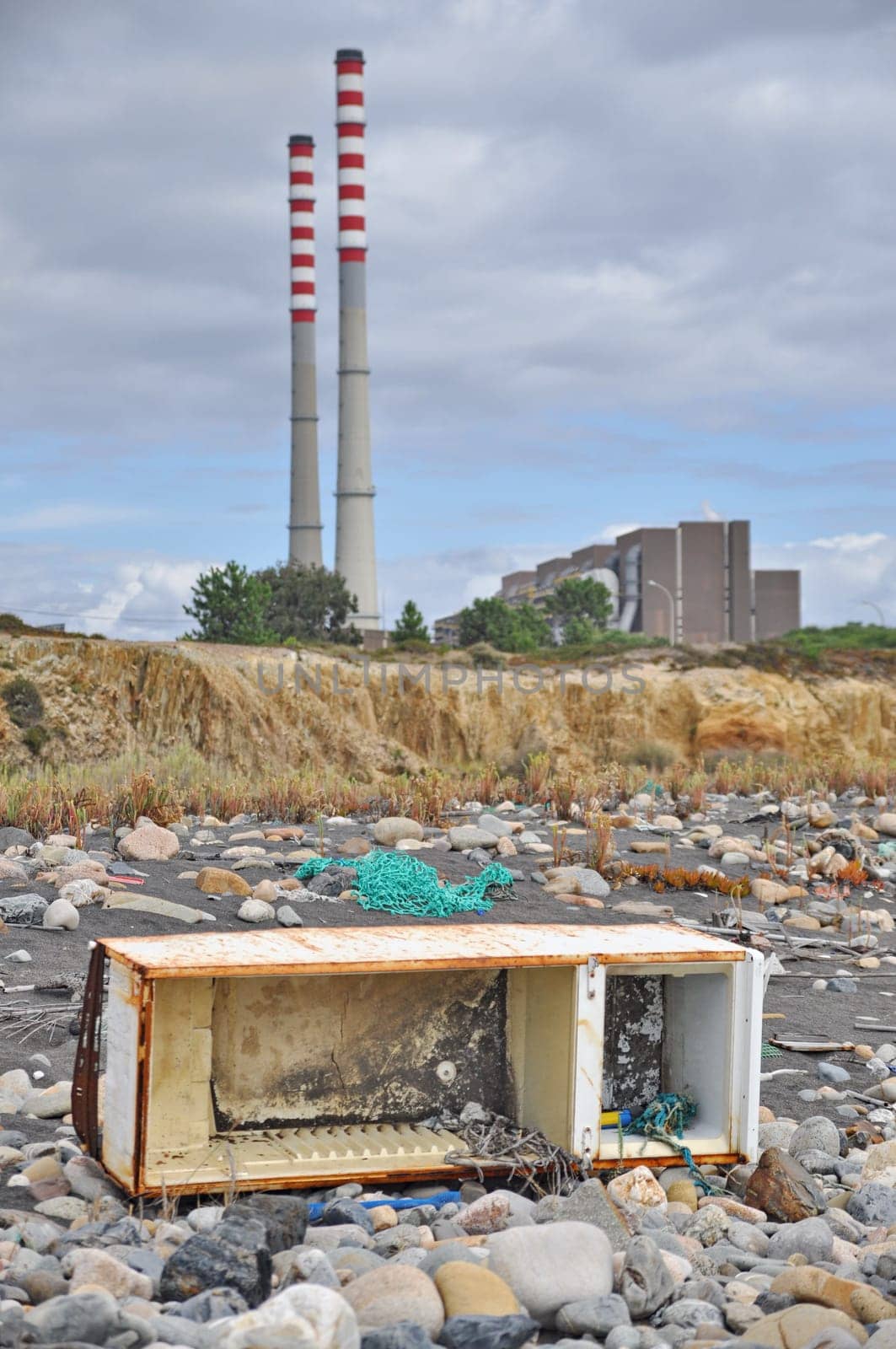 Trashed fridge on the seashore next to a factory