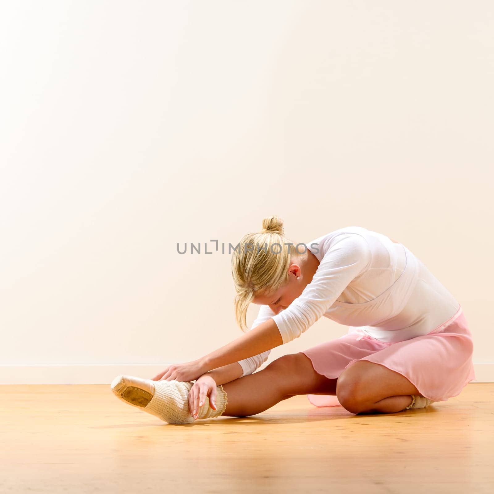 Beautiful ballerina warming up on the floor bending on knee