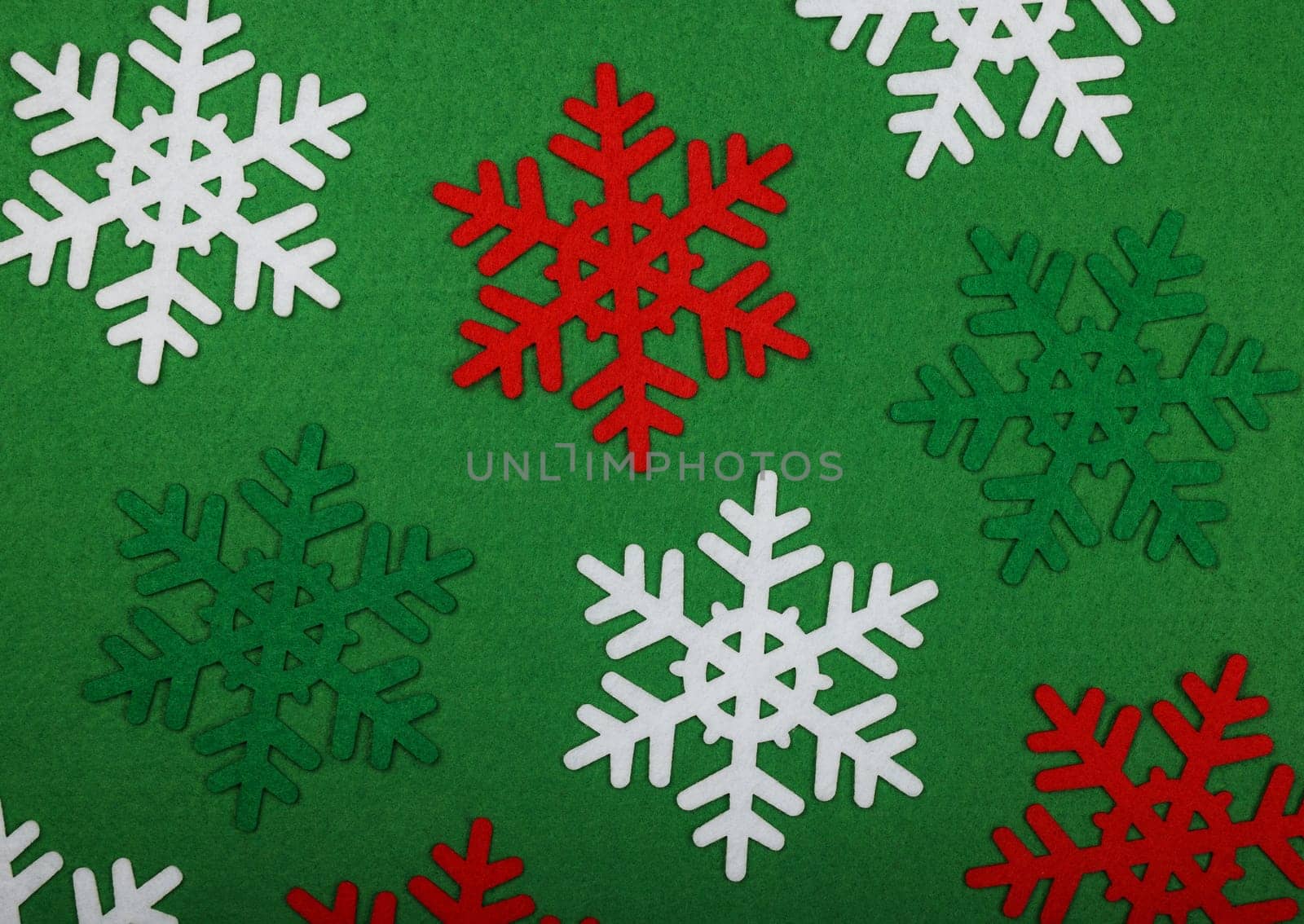 Close up pattern of red and white felt snowflakes Christmas decoration over green background, table top view, flat lay