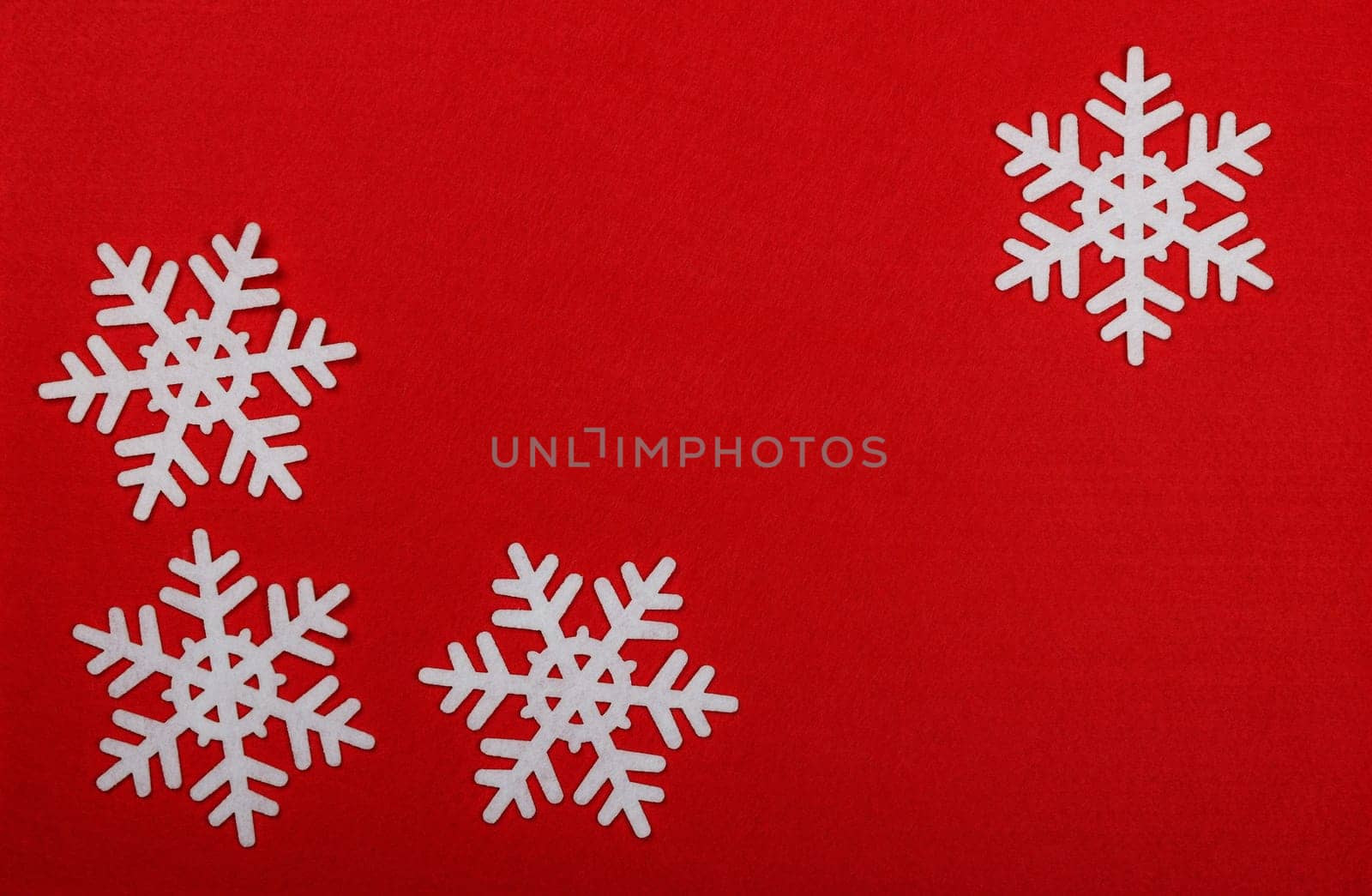 Close up pattern of white felt snowflakes Christmas decoration over red background, table top view, flat lay