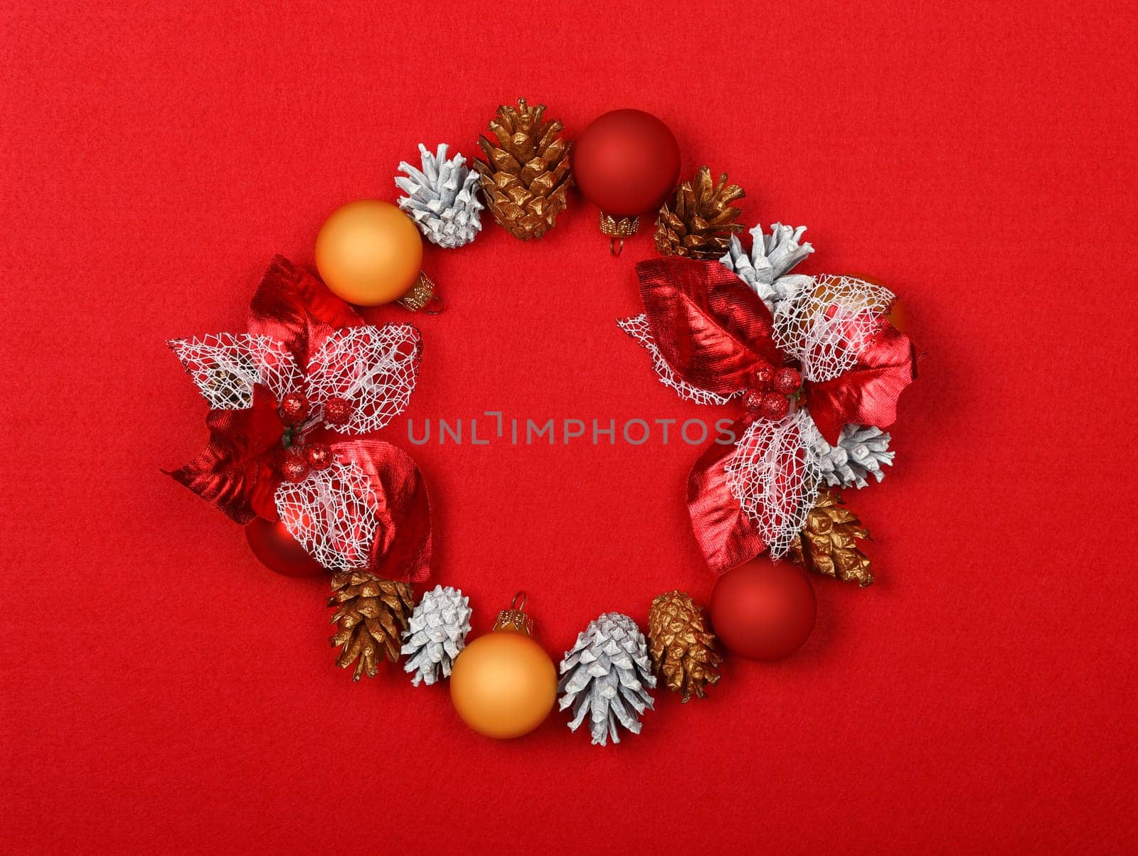 Close up Christmas wreath decoration of white and golden painted cones over red felt background with copy space, table top view, flat lay