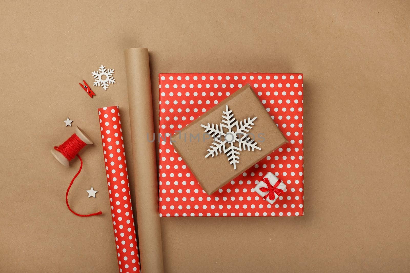 Close up flat lay of packing and wrapping Christmas gift boxes with red paper, table top view, directly above