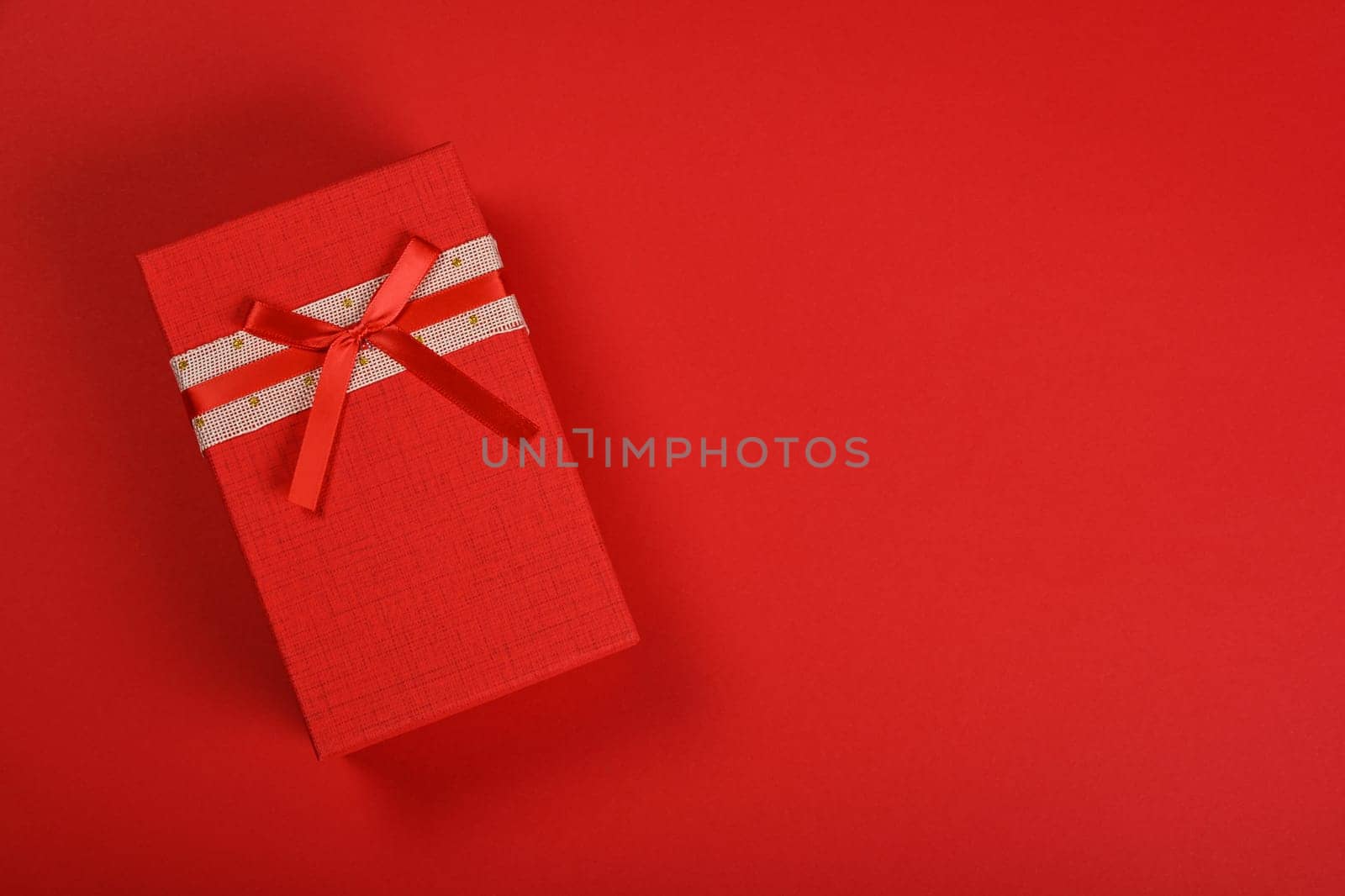 Valentine template of closed vivid red gift box with ribbon chiffon bow over red wrapping paper background, close up flat lay, elevated top view, directly above