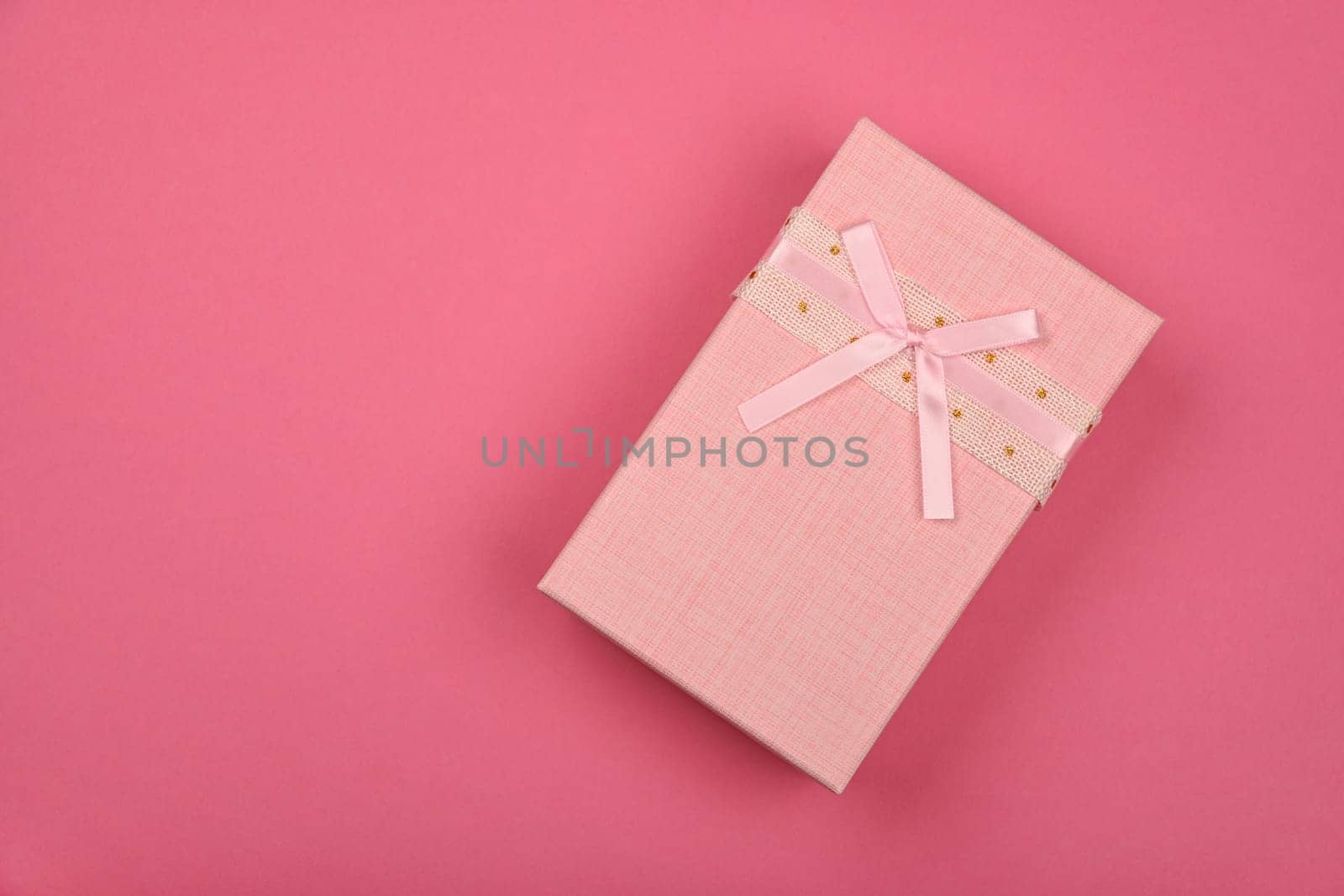 Valentine template of closed pastel pink gift box with ribbon chiffon bow over pink wrapping paper background, close up flat lay, elevated top view, directly above