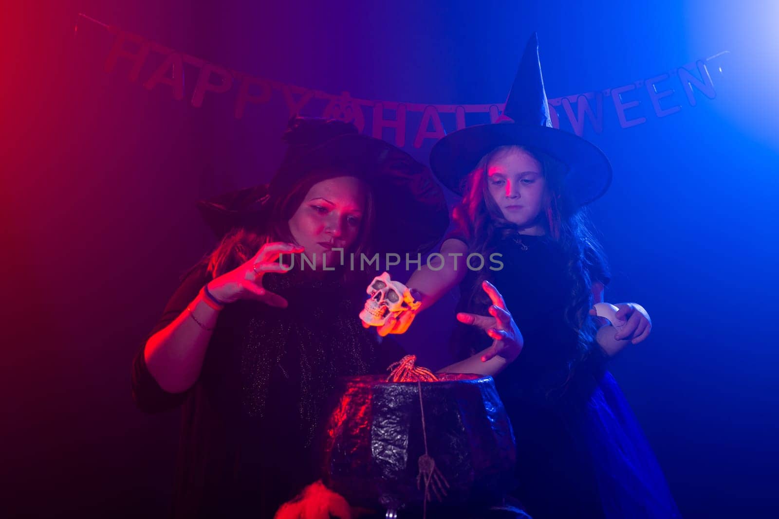 Funny child girl and woman in witches costumes for Halloween making magic. by Satura86