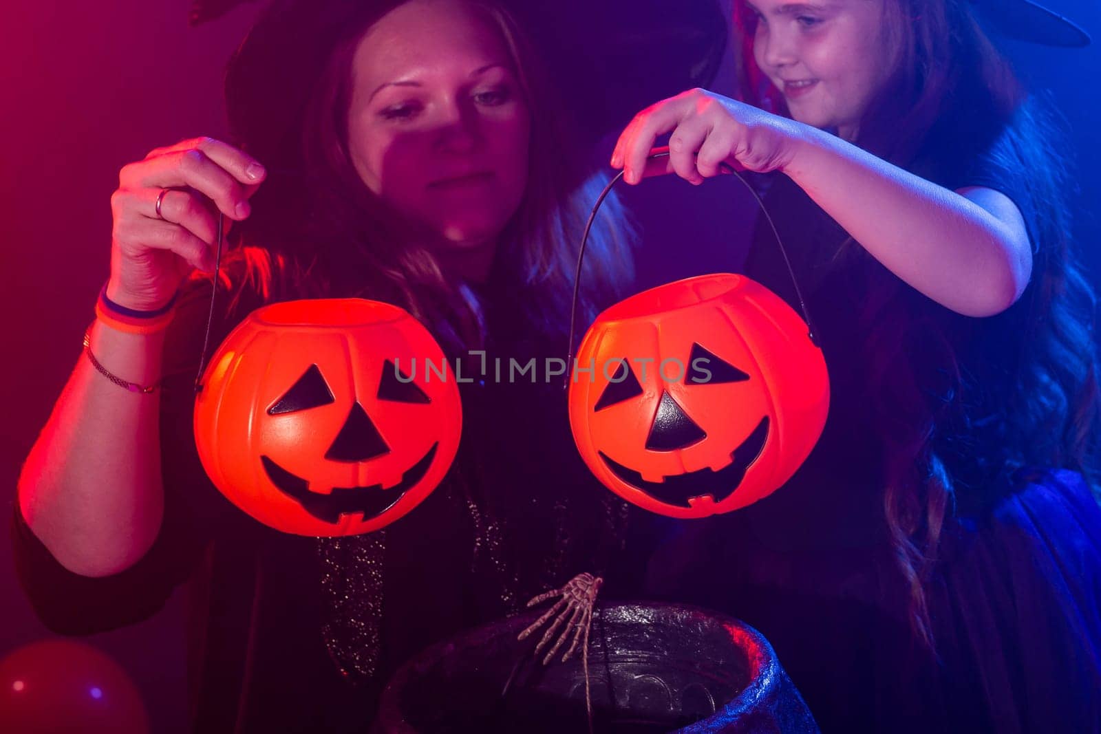 Funny child girl and woman in witches costumes for Halloween making magic with jack lantern close-up by Satura86