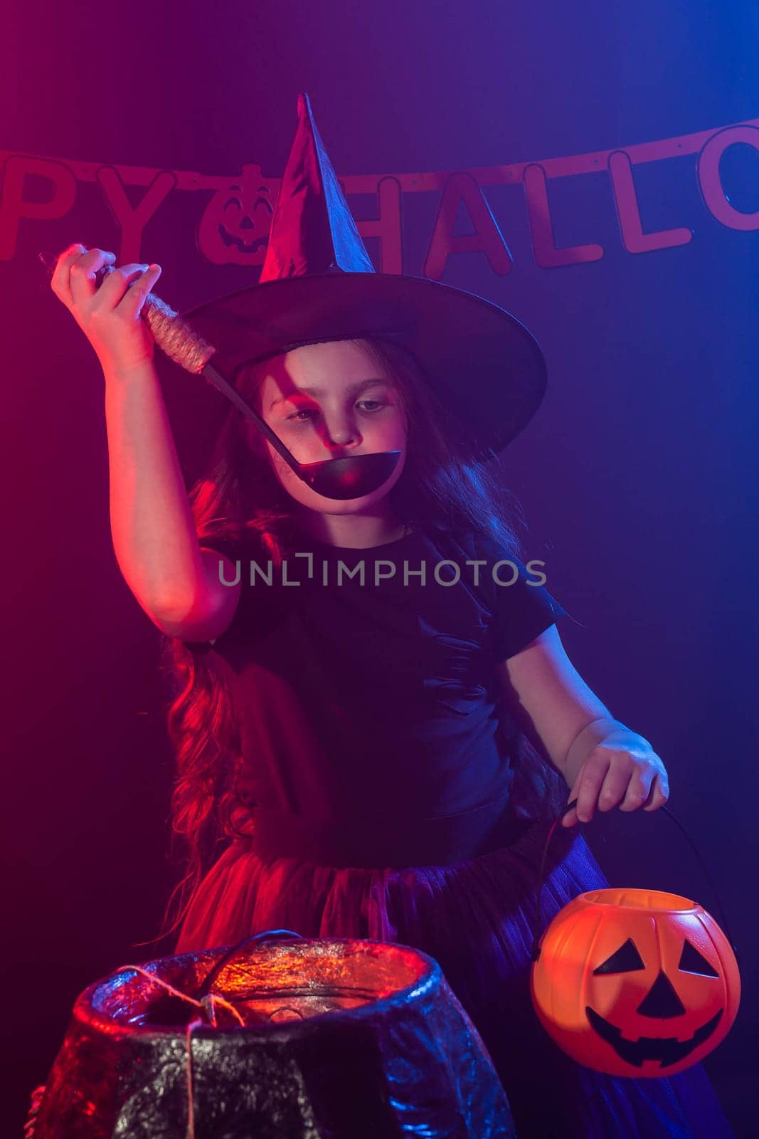 Child girl witch preparing a potion in the cauldron at halloween holidays