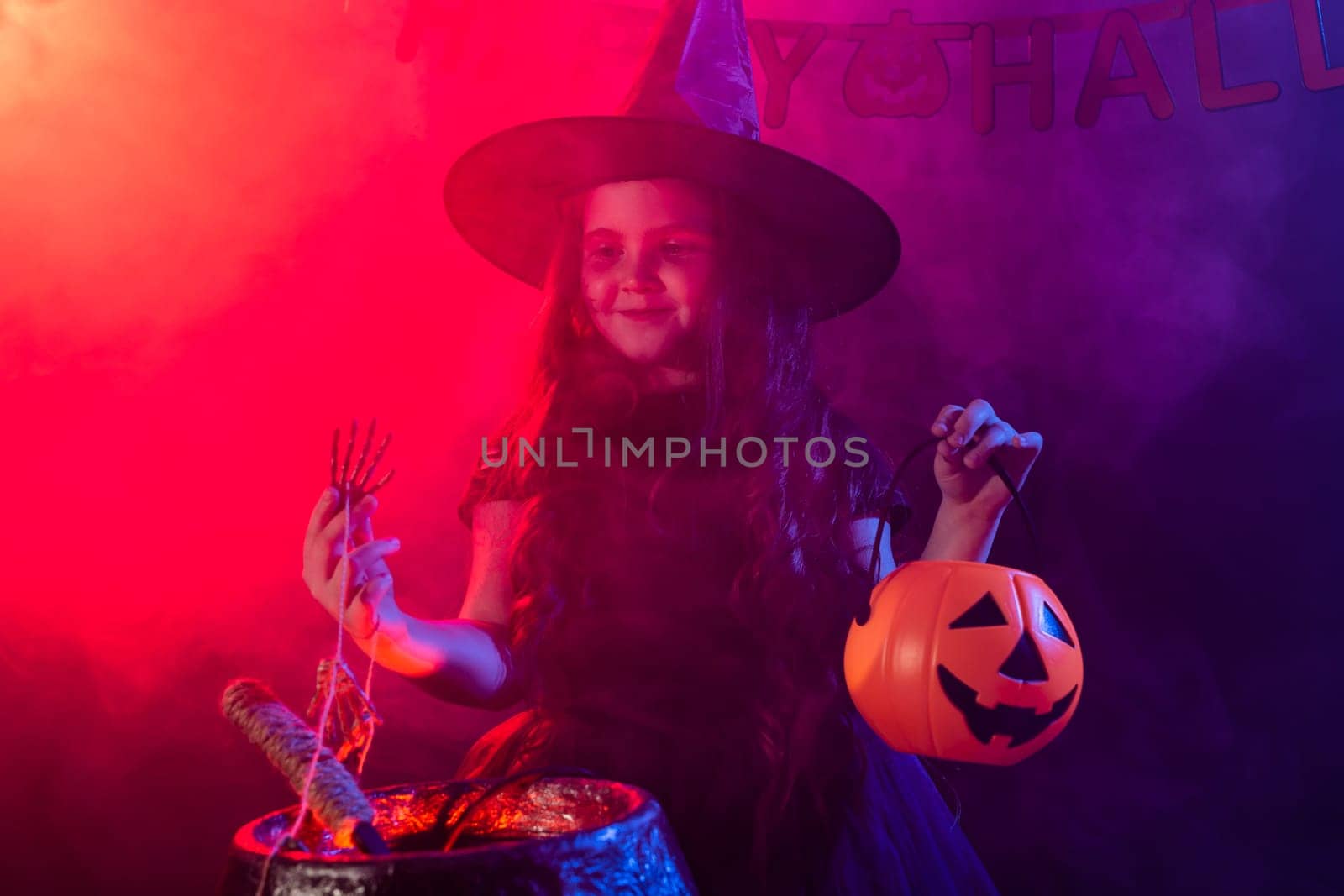 Child girl witch preparing a potion in the cauldron at halloween holidays