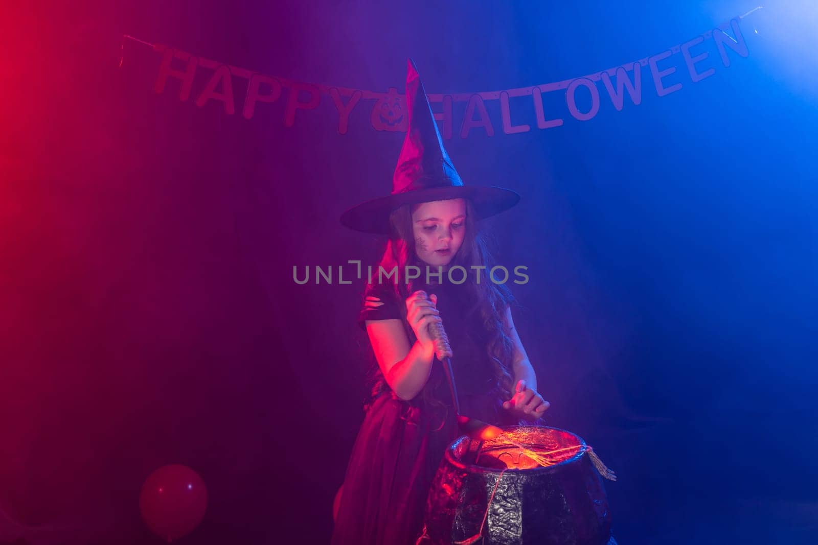 Little witch child cooking potion in the cauldron on Halloween