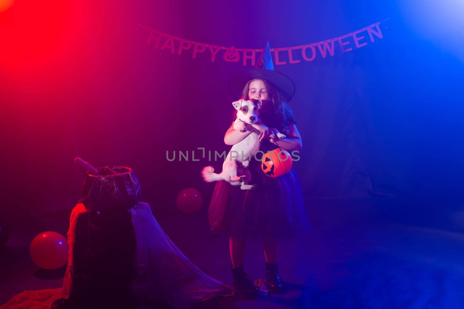 Funny child girl in witch costume for Halloween with pumpkin Jack and dog