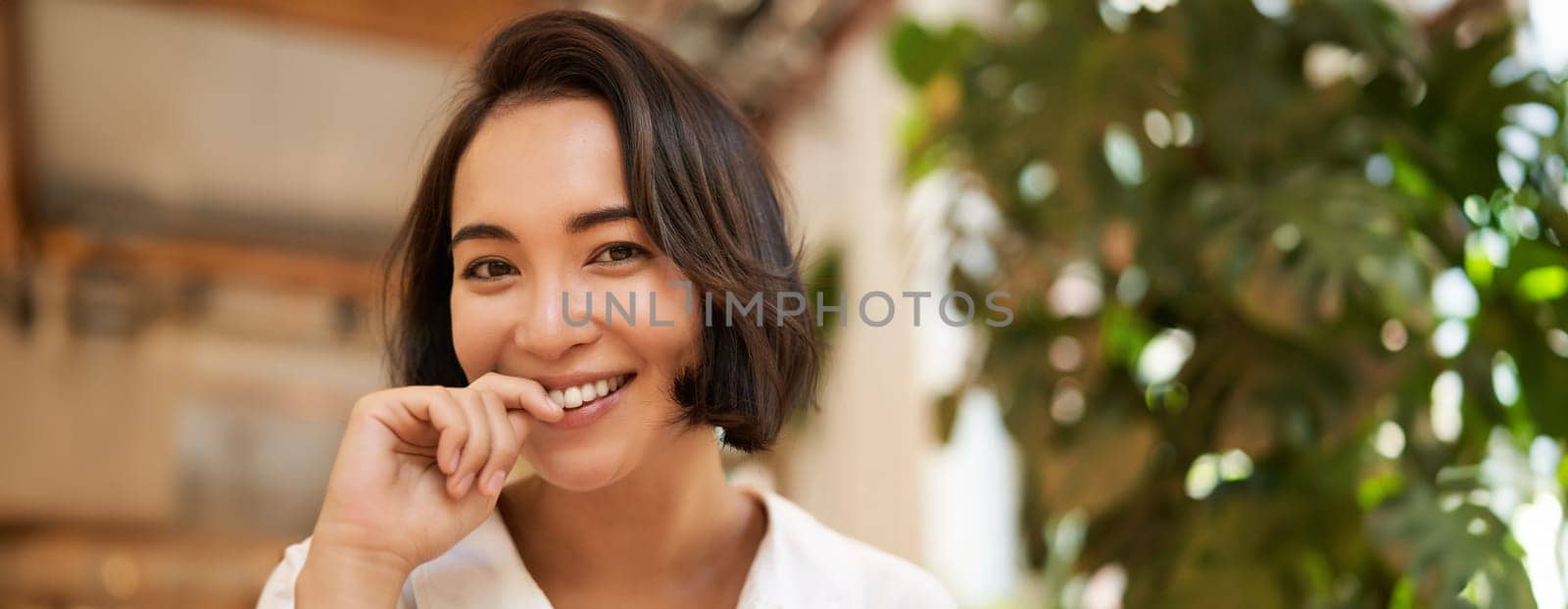 Close up portrait of beautiful brunette asian girl, smiling and looking flirty at camera, chuckle cute. Copy space