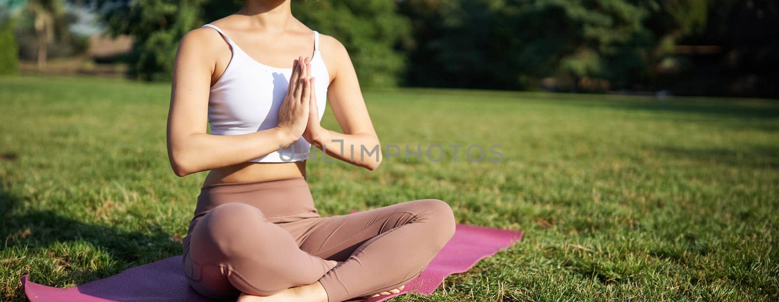 Woman meditating on lawn in park, sitting on sports mat, relaxing, breathing fresh air.